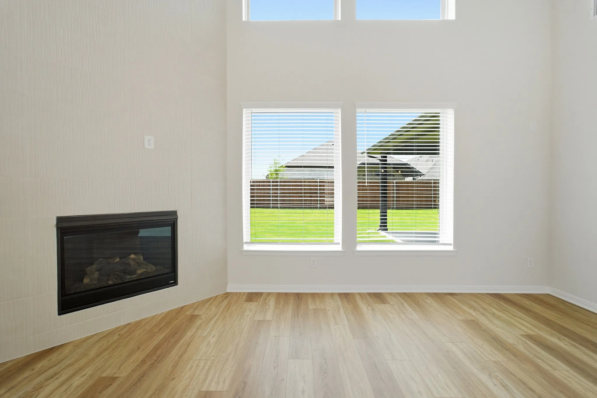 Spacious living area featuring high ceilings, wood-finish flooring, and an integrated fireplace with a tiled surround