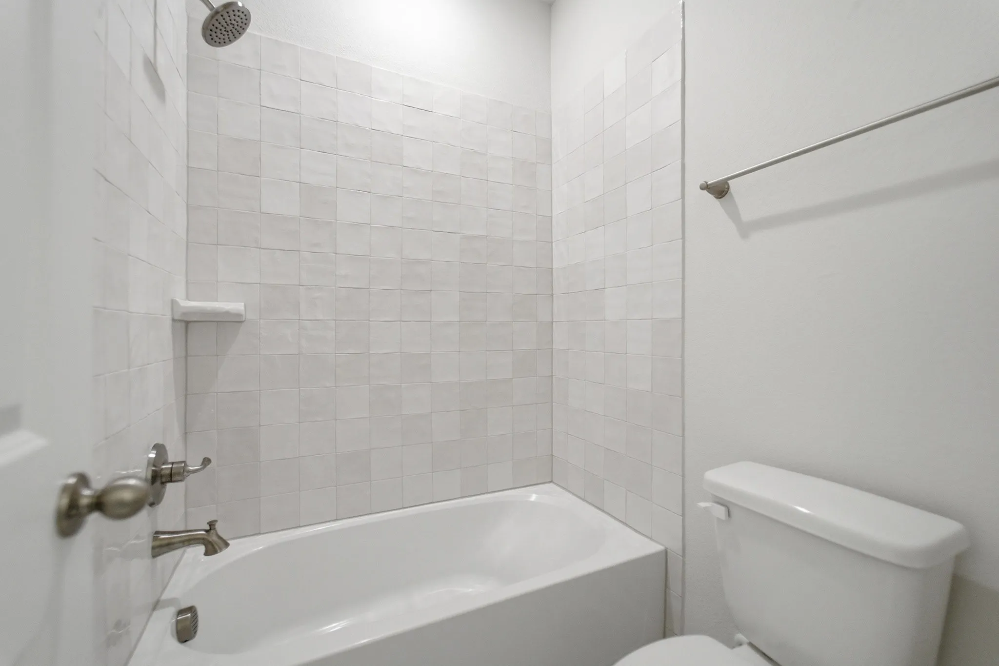 Full-size bathtub with a tile surround, featuring a built-in soap dish, brushed nickel fixtures, and a coordinating showerhead