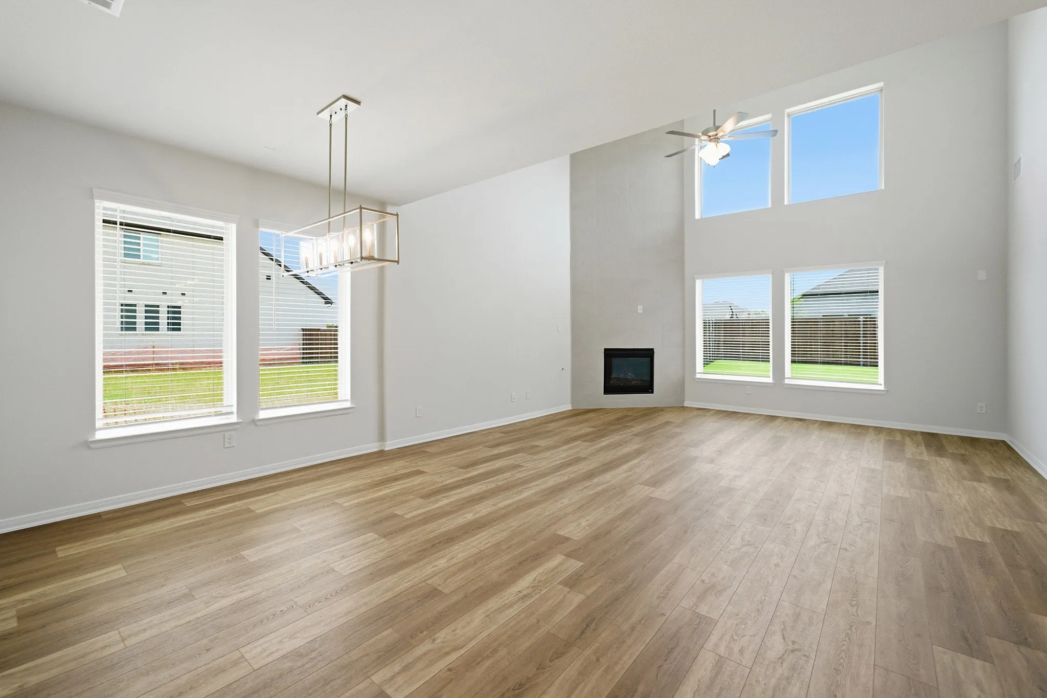 Spacious living area featuring high ceilings, wood-finish flooring, a contemporary fireplace, and multiple large windows with blinds
