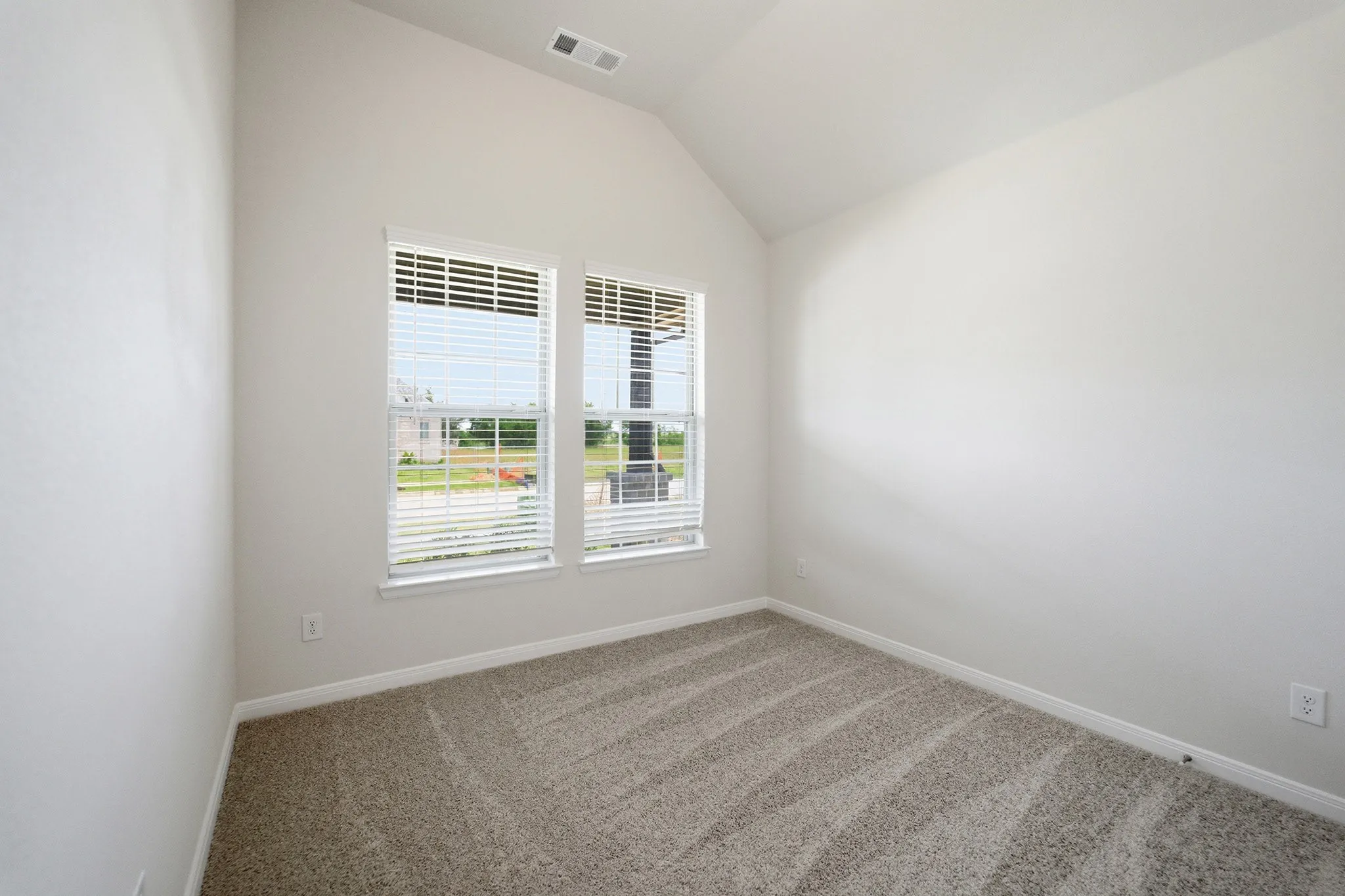 Interior room featuring vaulted ceilings, light-toned carpeting, dual windows with blinds, and white wall finishes