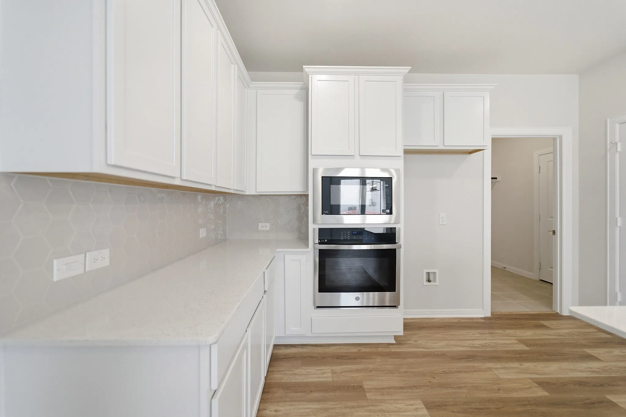 Kitchen featuring white cabinetry, light-toned countertops, a light gray hexagonal tile backsplash, and stainless steel built-in appliances