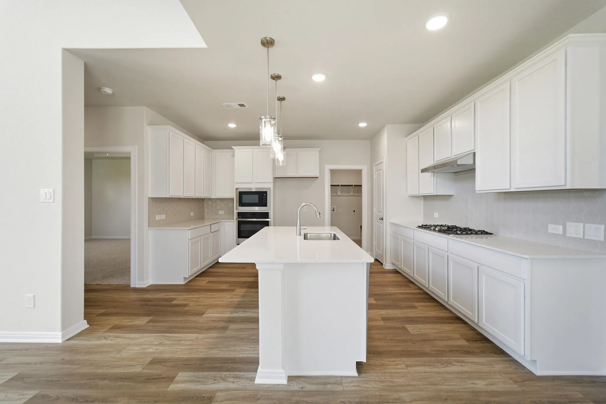 Contemporary kitchen featuring an expansive center island with an undermount sink, white cabinetry, integrated stainless steel appliances, and wood-finish flooring