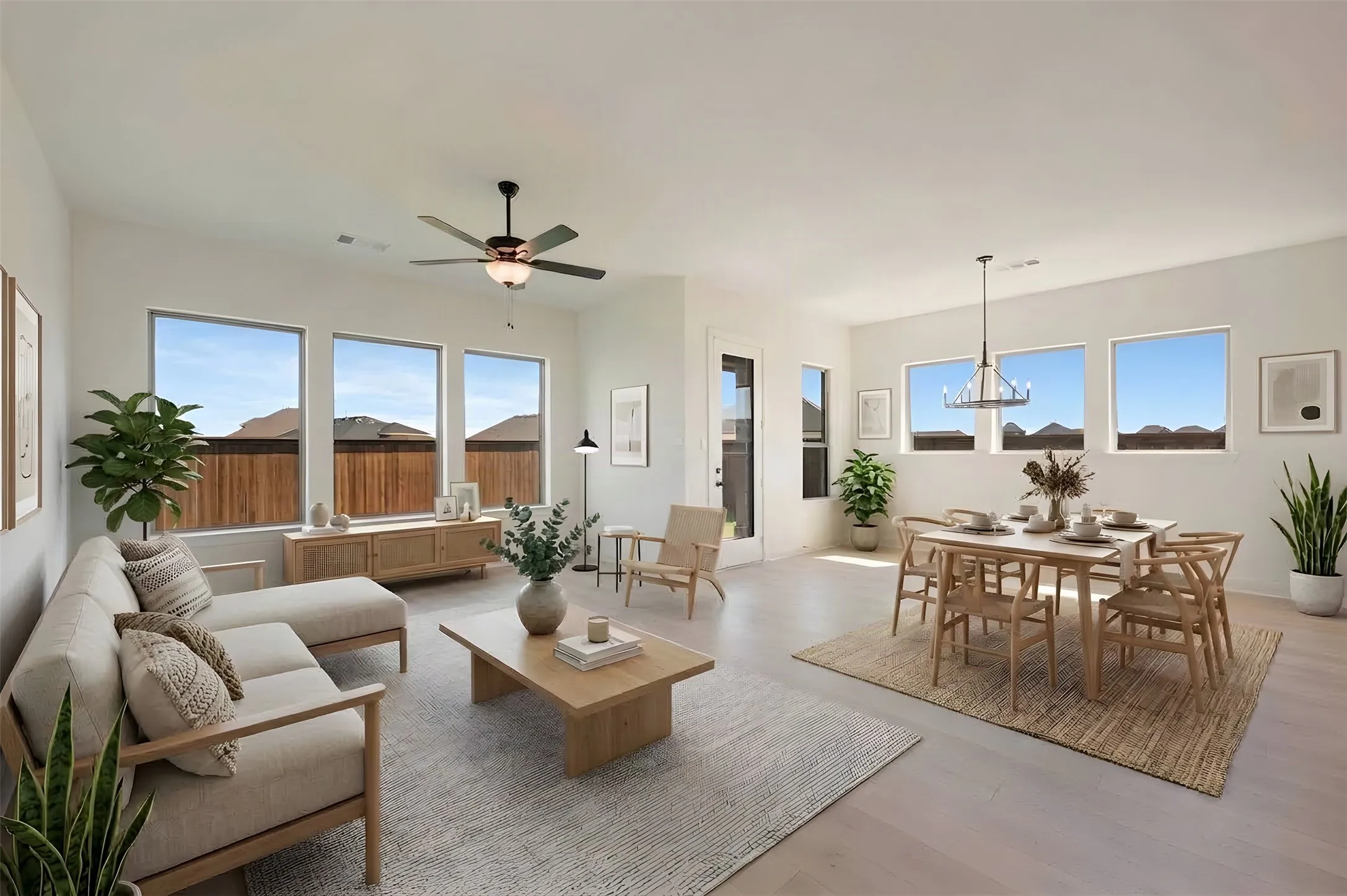 Open-concept living space featuring light wood-finish flooring, multiple windows, a ceiling fan, and a modern chandelier