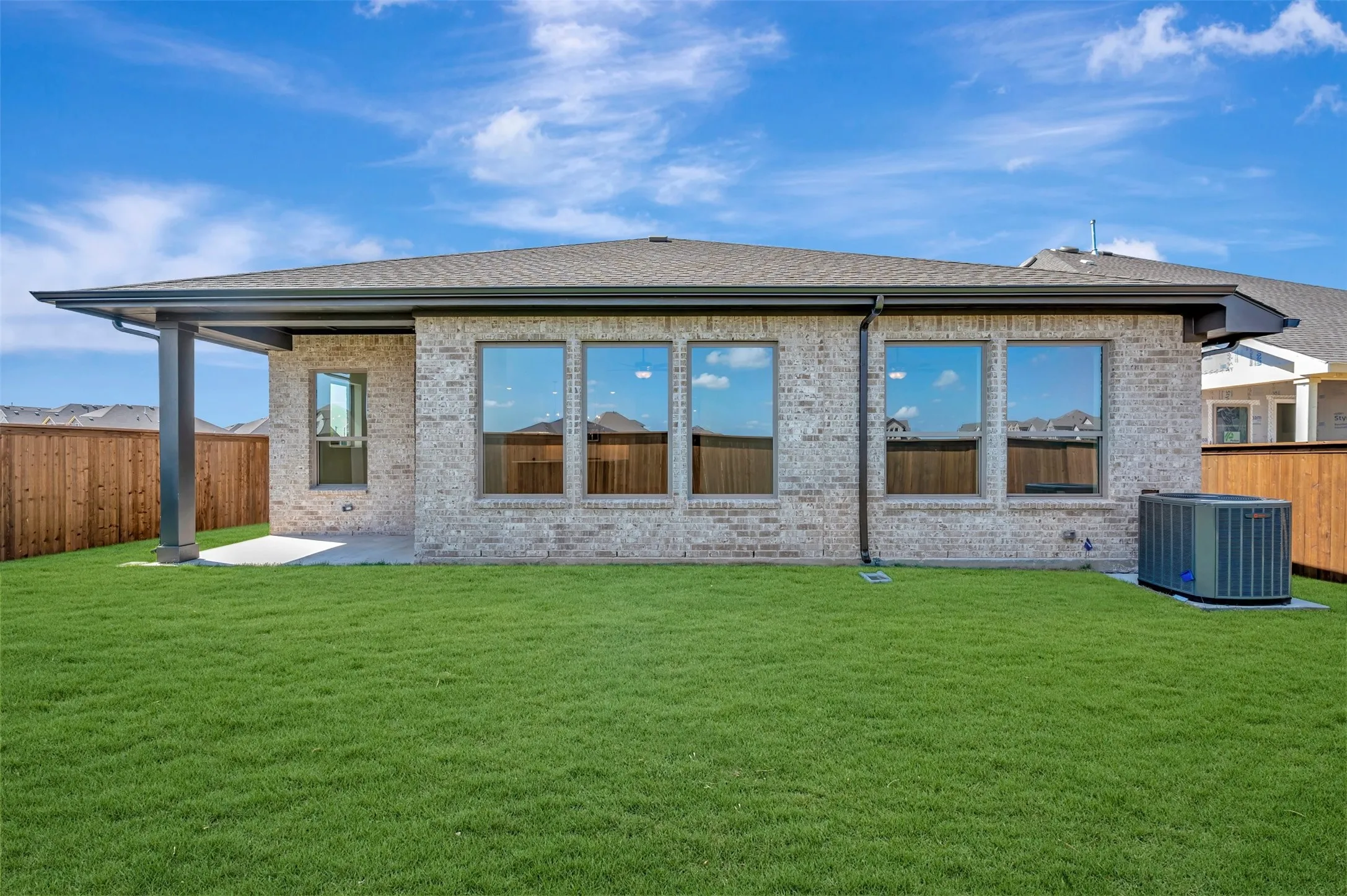 Expansive green lawn, brick exterior, covered patio, dark framed windows, and a privacy fence