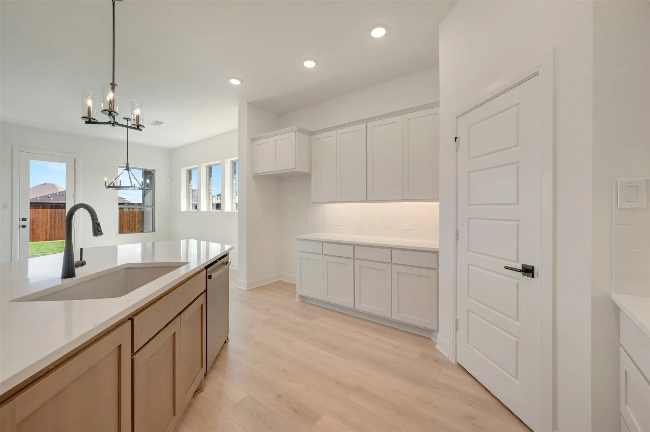 Modern kitchen featuring light wood-finish flooring, white cabinetry with under-cabinet lighting, a central island with an integrated sink and gooseneck faucet, and stainless steel appliances