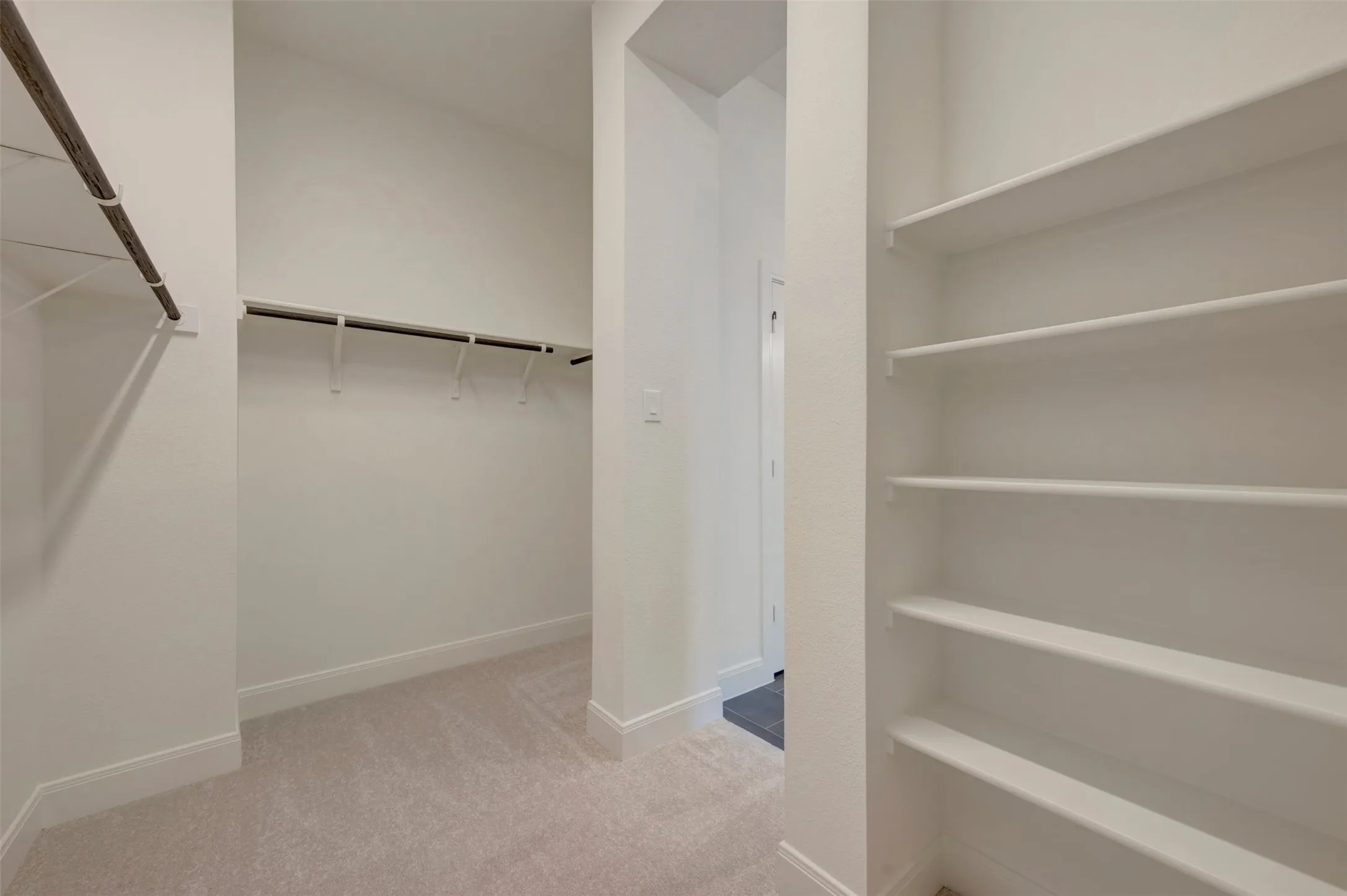Carpeted walk-in closet featuring multiple hanging rods and built-in shelving