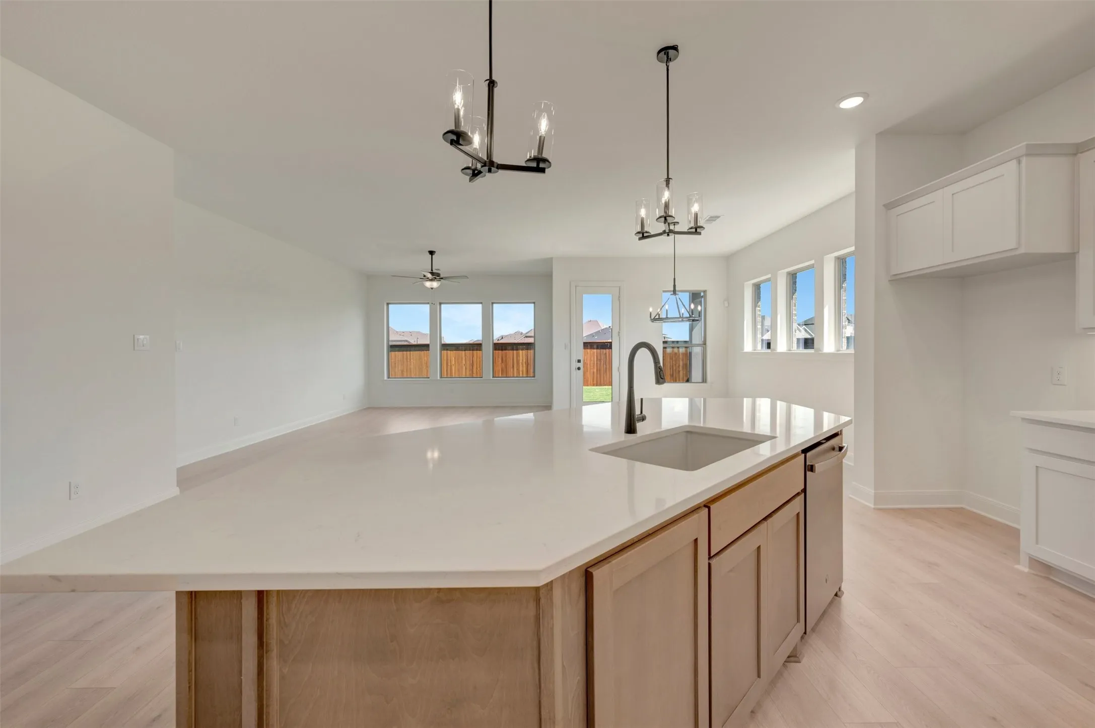 Spacious open-concept interior with light wood-finish flooring, recessed lighting, and multiple large windows