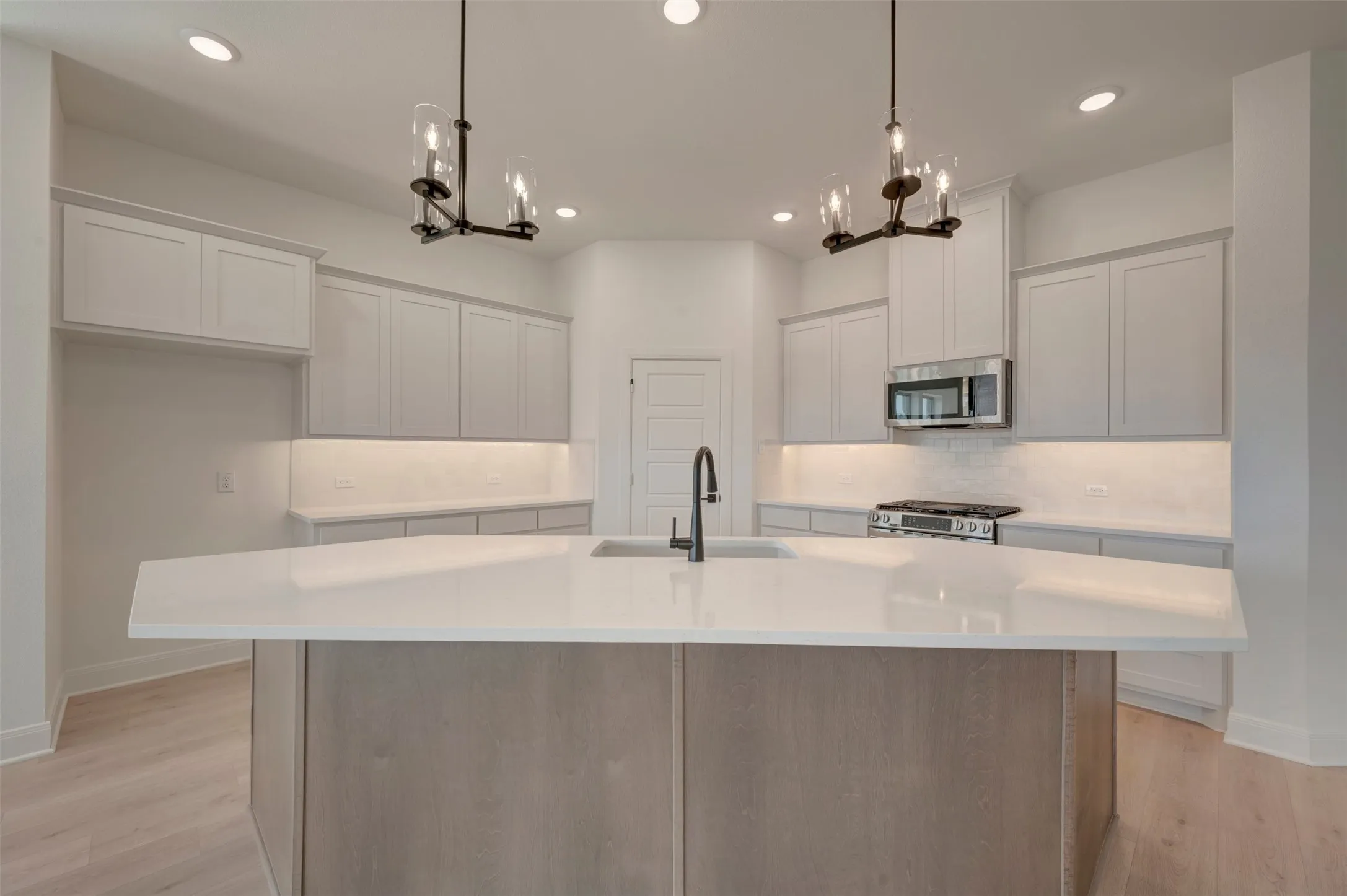 Spacious kitchen featuring a large central island with an integrated sink, light-toned cabinetry, stainless steel appliances, and wood-finish flooring
