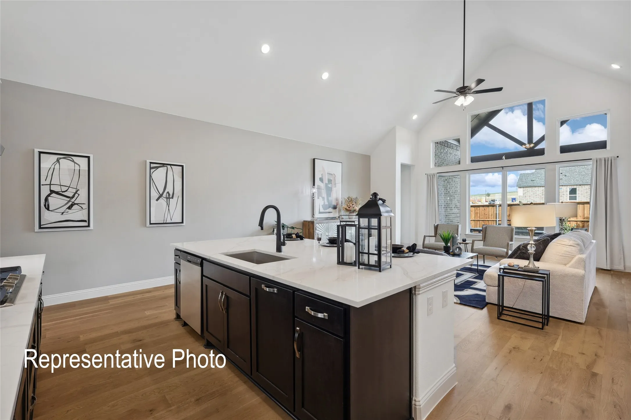 Open-concept living space featuring a central kitchen island with a built-in sink, dark cabinetry, and light-toned countertops