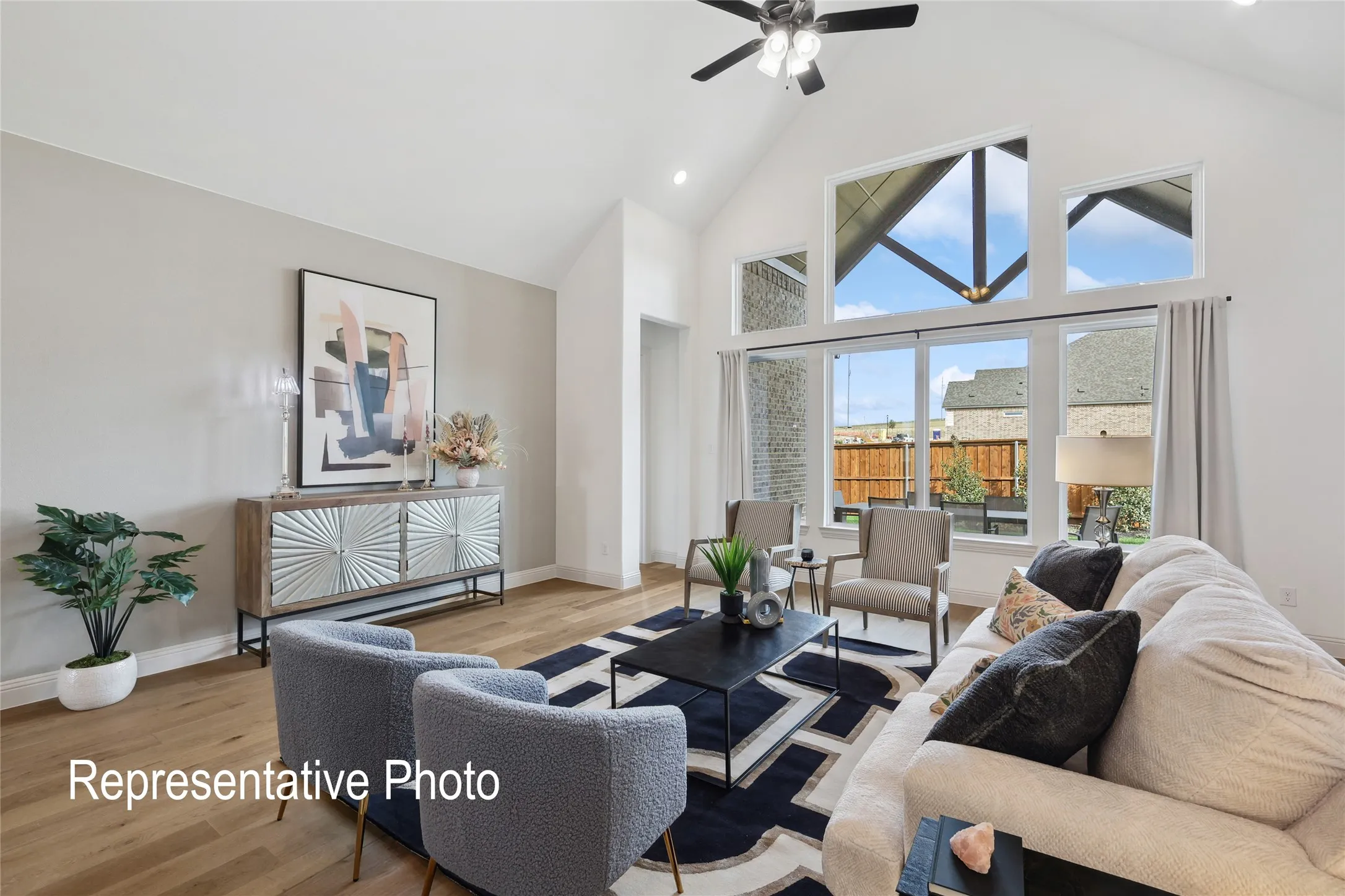 Open-concept living space featuring a vaulted ceiling with a ceiling fan, wood-finish flooring, and expansive windows with transoms