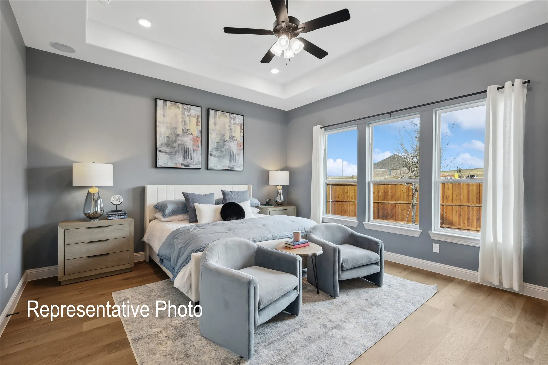 Bedroom featuring wood-finish flooring, a tray ceiling with recessed lighting and ceiling fan, and a trio of windows with white trim