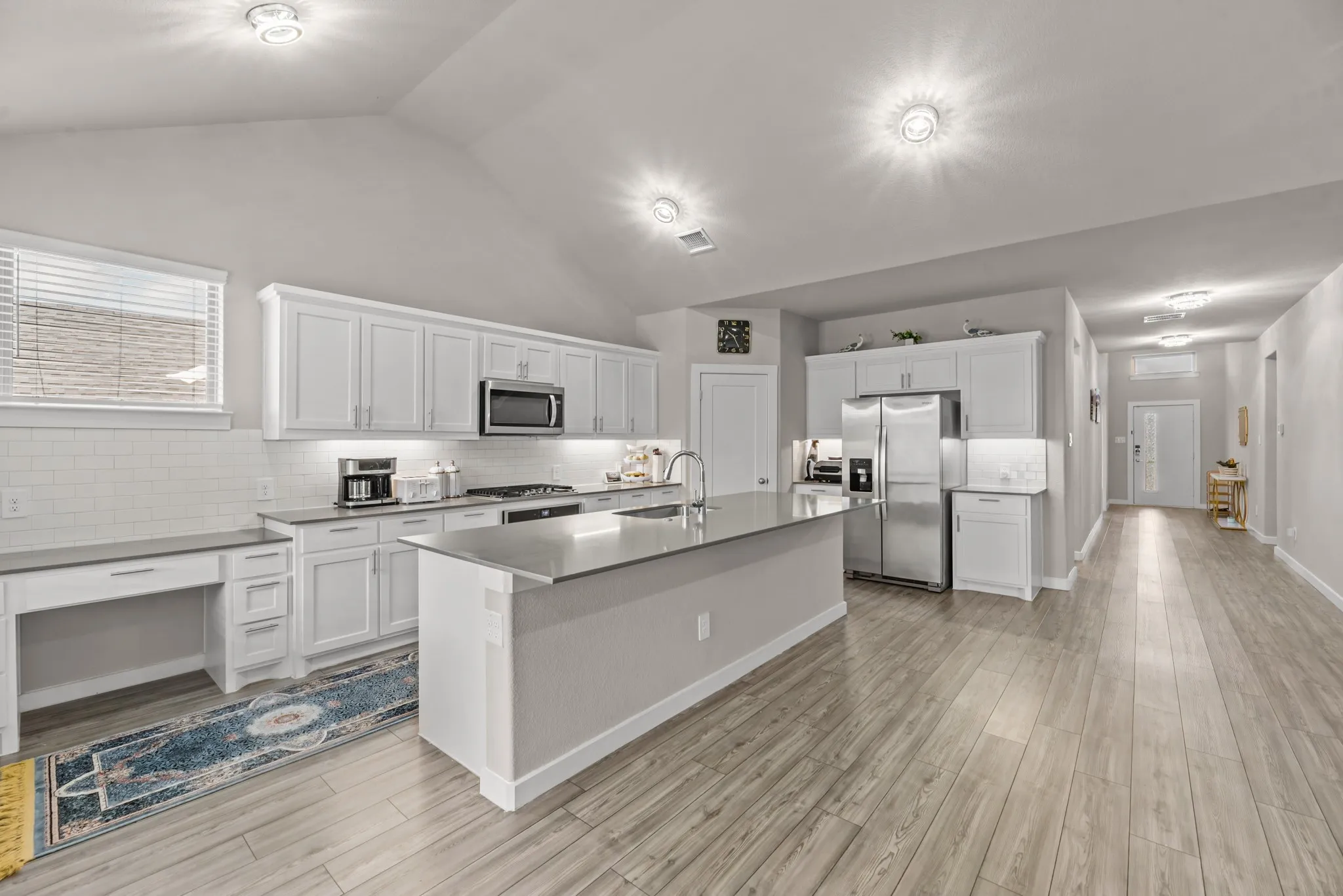 Spacious kitchen featuring an expansive center island, abundant white cabinetry, stainless steel appliances, and wood-finish flooring