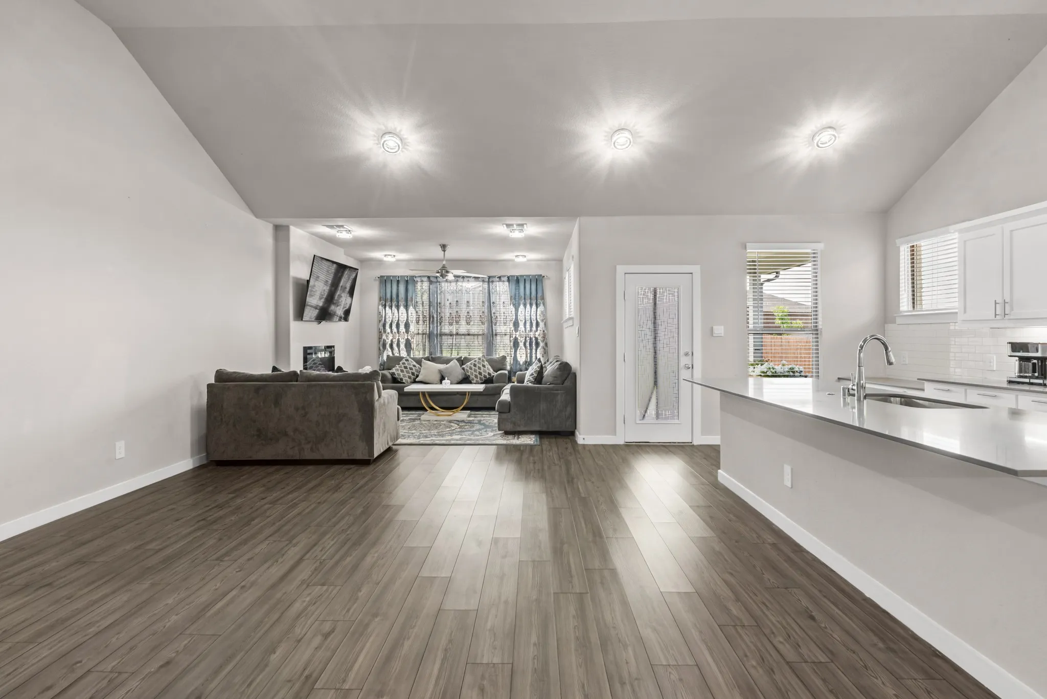 Spacious open-concept living area featuring wood-finish flooring, vaulted ceilings, and recessed lighting