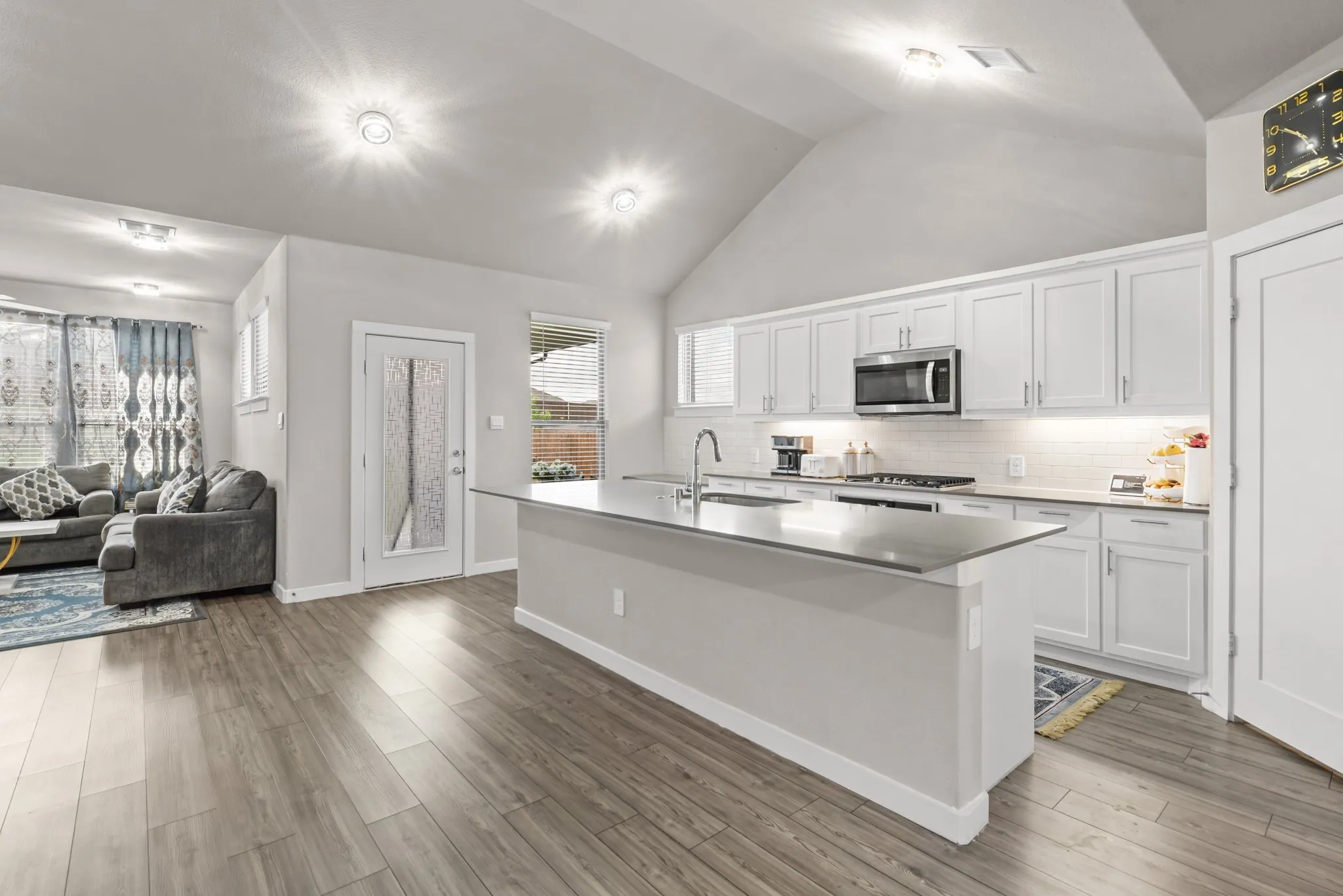 Modern kitchen featuring white shaker cabinetry, stainless steel appliances, a large island with sink, subway tile backsplash, and vaulted ceilings