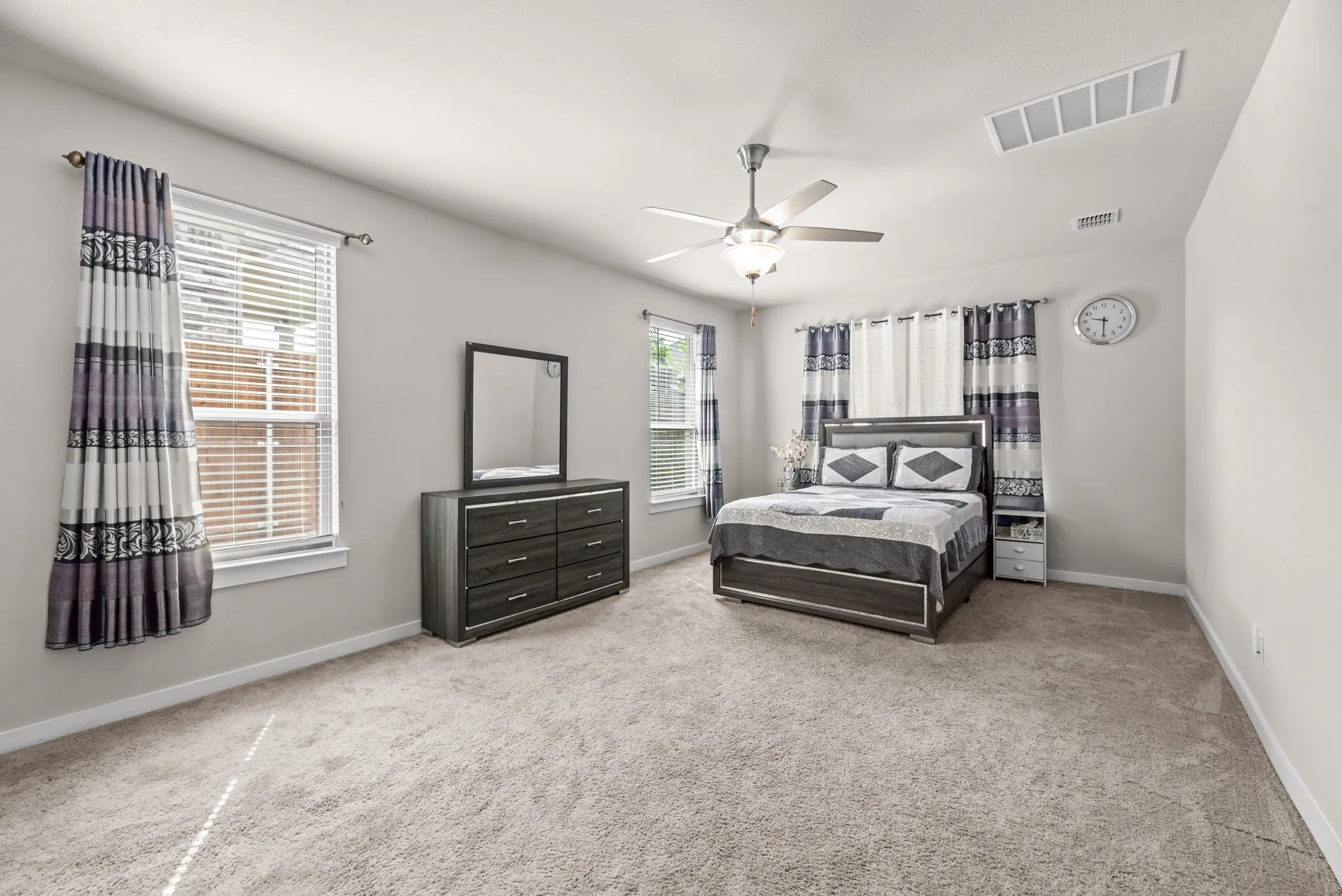 Carpeted room featuring multiple windows with blinds, a ceiling fan with integrated lighting, and neutral wall tones
