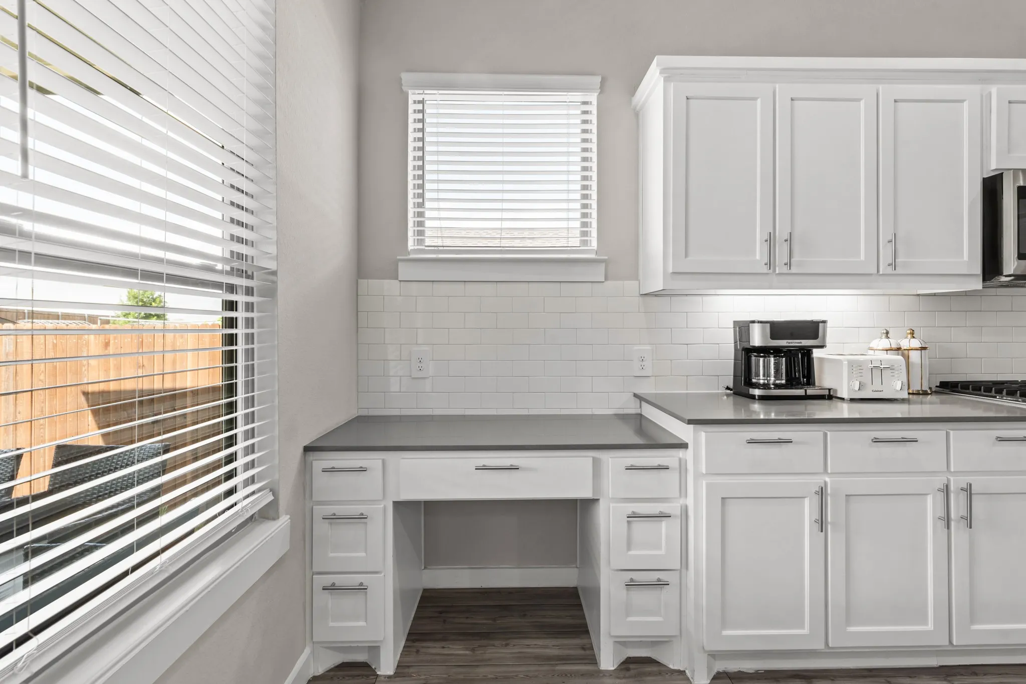 Kitchen workspace featuring white shaker-style cabinetry, dark countertops, and white subway tile backsplash