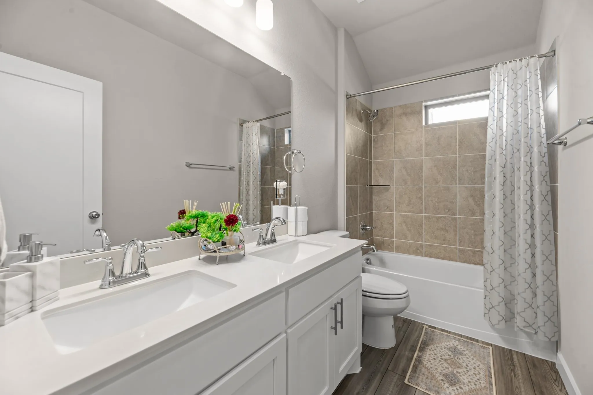 Bathroom featuring a dual vanity with undermount sinks, wood-finish flooring, a full-width mirror, a tiled shower-tub combination, and a horizontal window