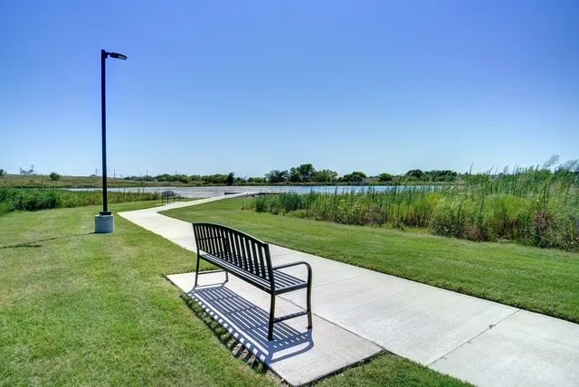 Winding concrete pathway with a black metal bench, bordered by manicured green grass and natural water features