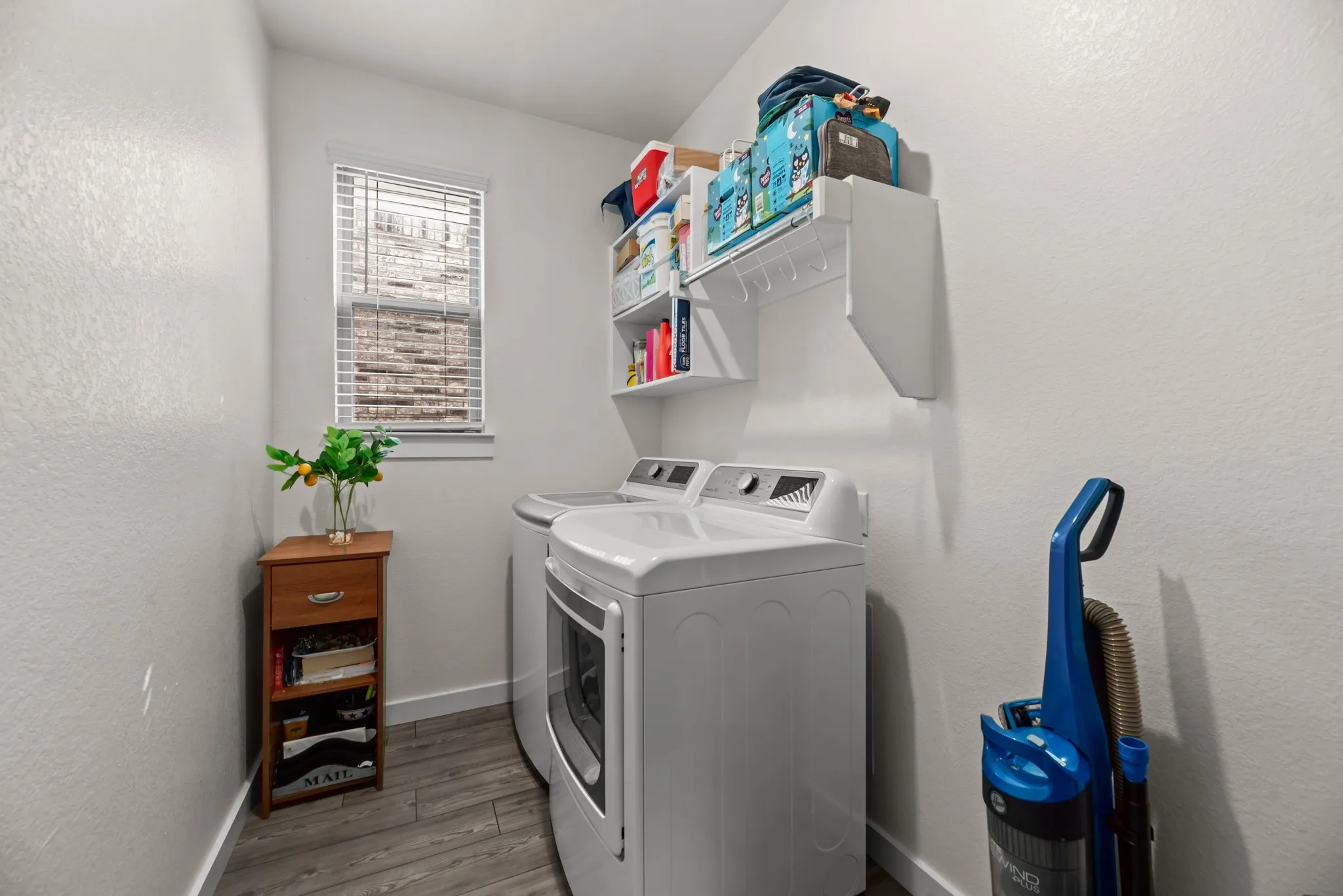 Dedicated laundry area featuring wood-finish flooring, a window with blinds, and built-in shelving for organization