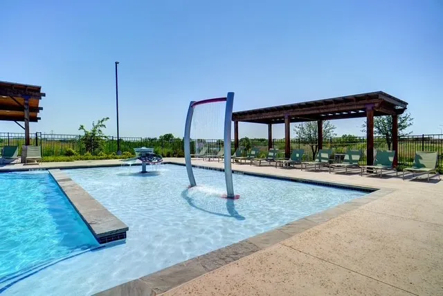 Expansive outdoor swimming pool featuring an integrated splash pad with a fountain and water curtain