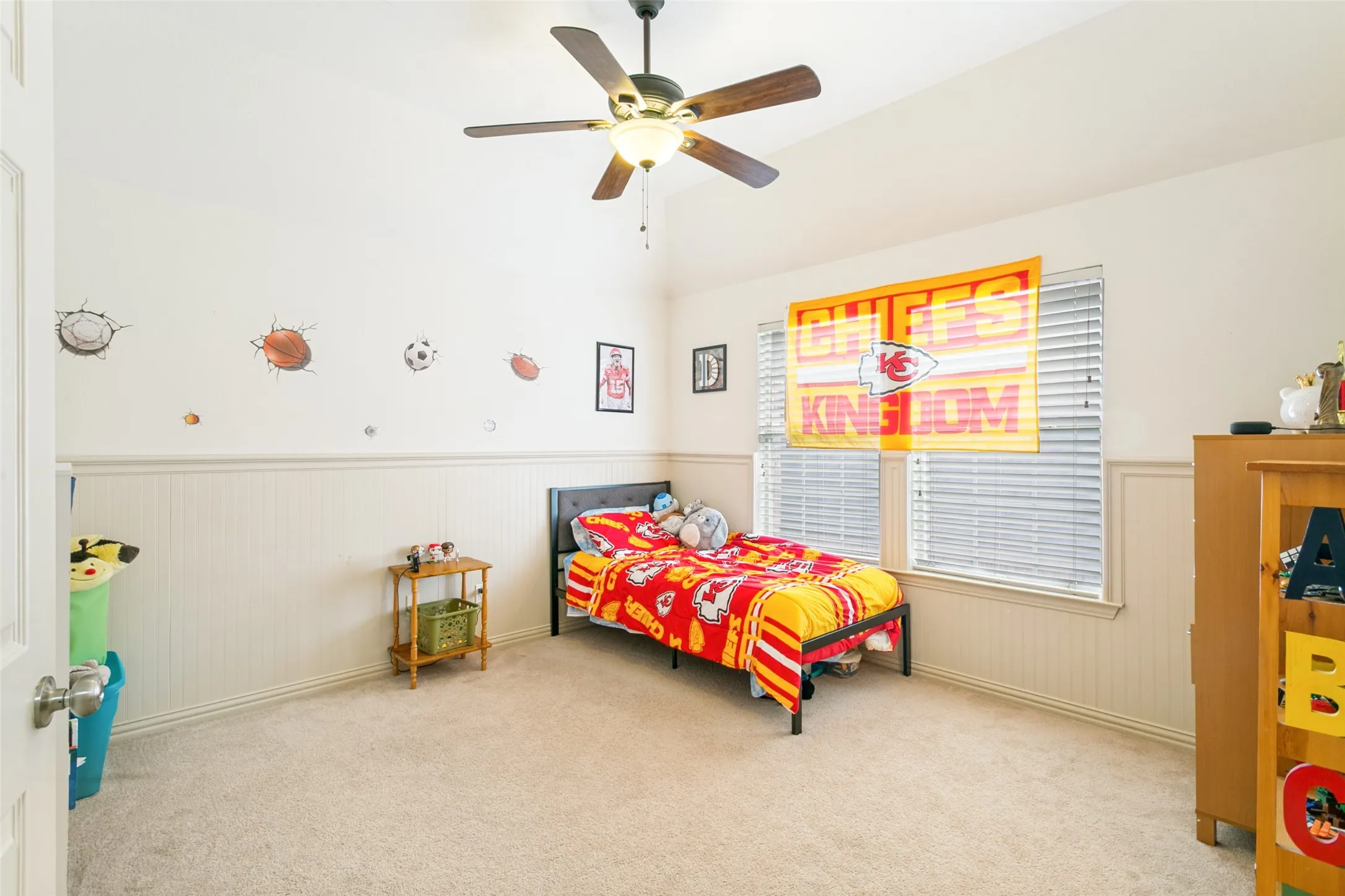 Carpeted interior space featuring wainscoting, an angled ceiling, and a ceiling fan with integrated lighting
