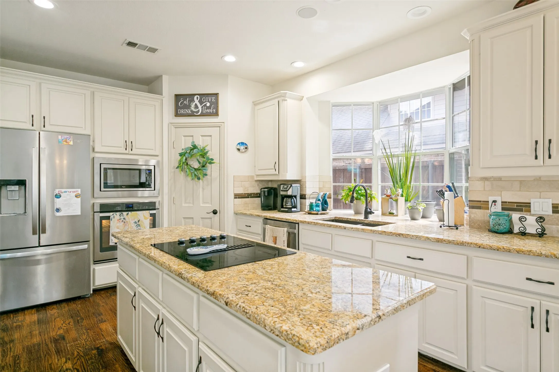 Kitchen featuring a central island with a built-in cooktop, white perimeter cabinetry, and wood-finish flooring