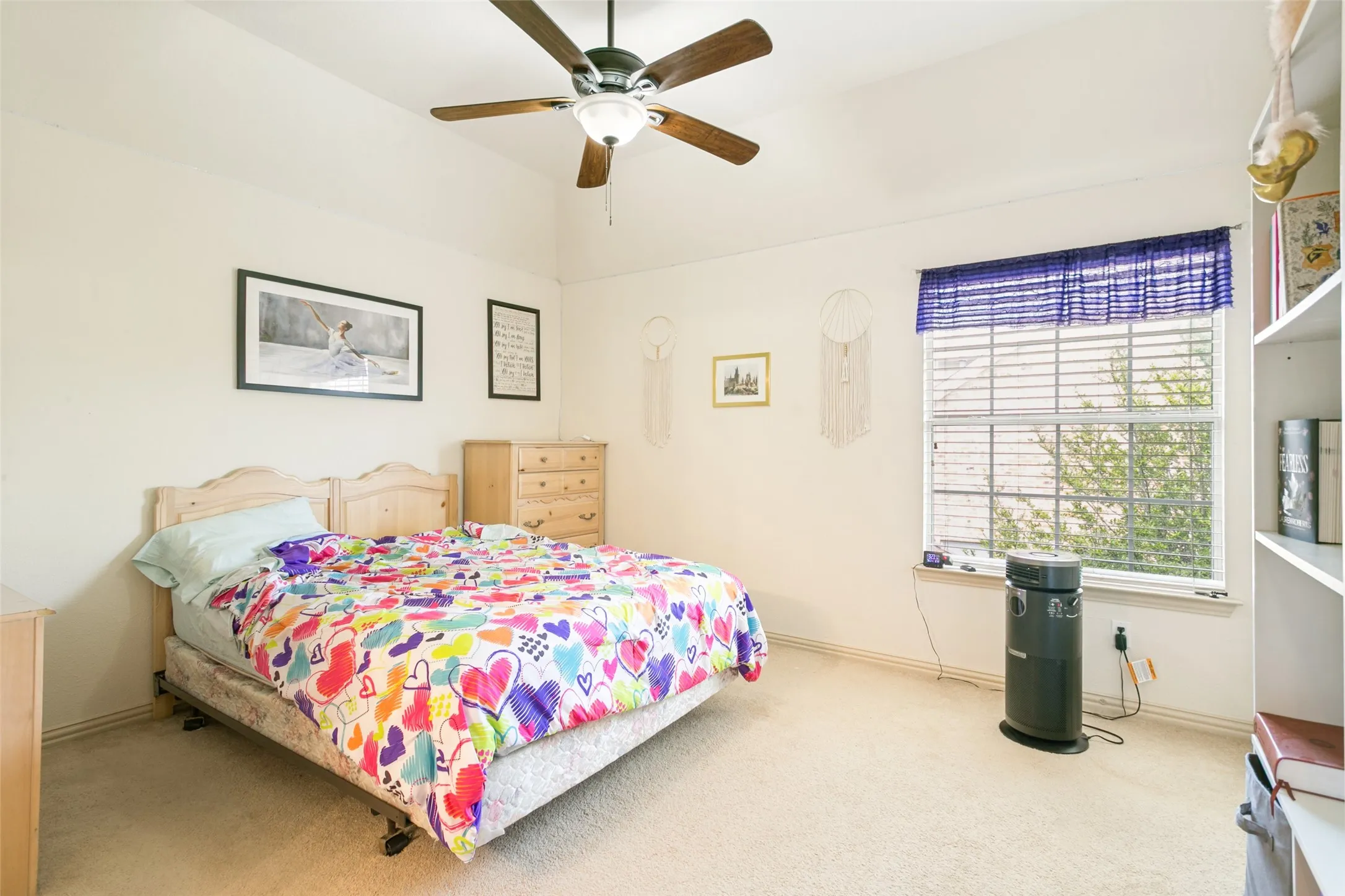 Carpeted room featuring a ceiling fan with light fixture, natural light from a window with blinds, and built-in shelving