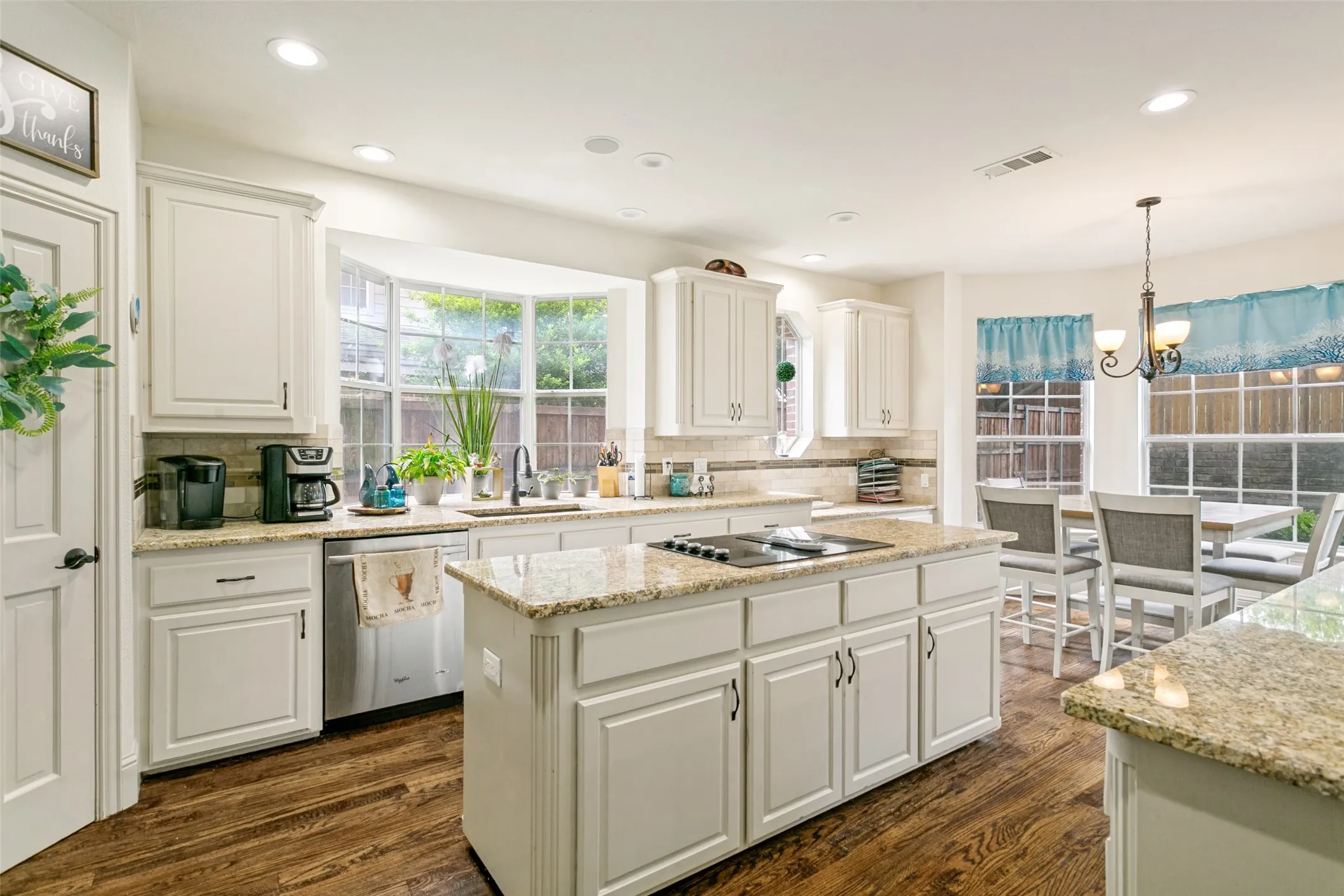 Kitchen featuring white cabinetry, granite countertops, wood-finish flooring, a bay window, and a central island with a built-in cooktop