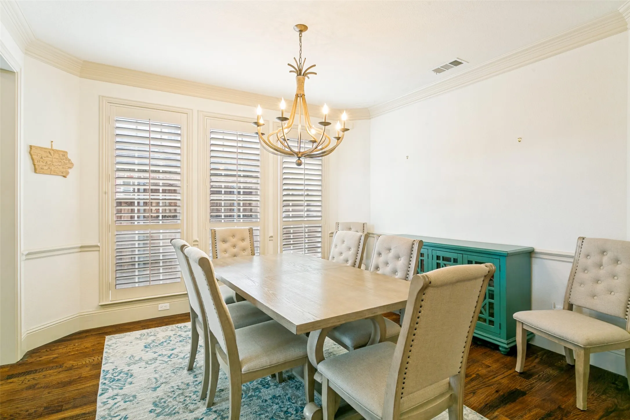 Bay window with plantation shutters, crown molding, chair rail detailing, wood-finish flooring, and a decorative chandelier