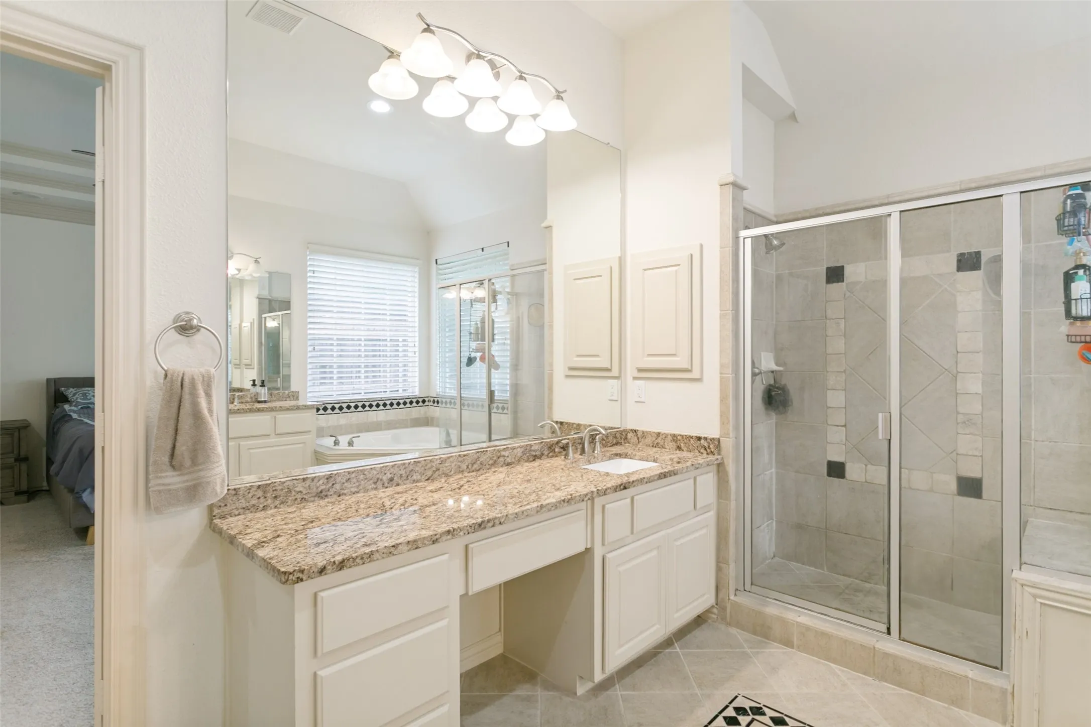 Spacious bathroom featuring a double vanity with stone countertops, a built-in makeup area, a large walk-in shower with tile surround, a soaking tub with tile accent, and a large wall-mounted mirror