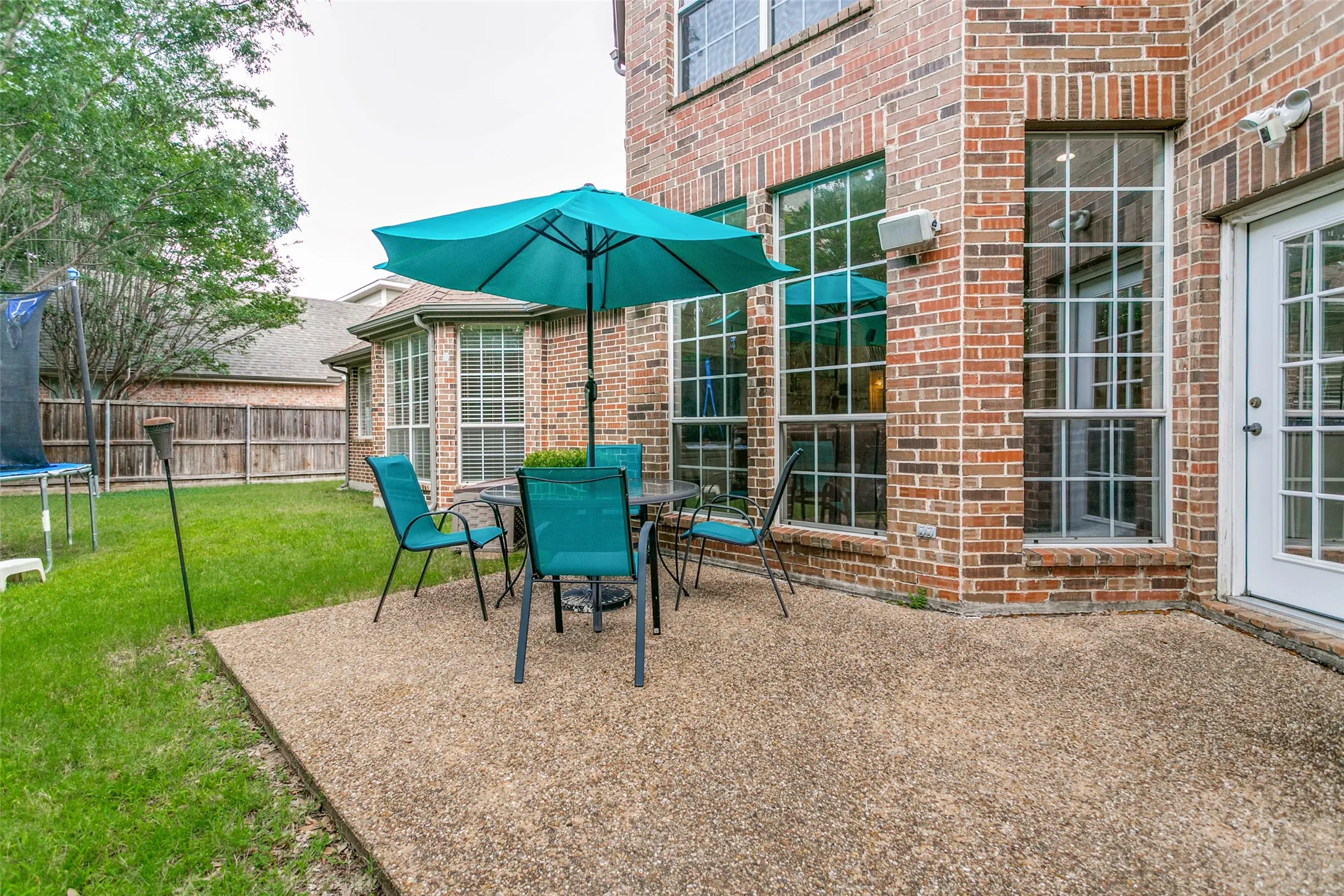 Expansive backyard featuring a large exposed aggregate patio, a brick exterior, multiple windows, and a white French door