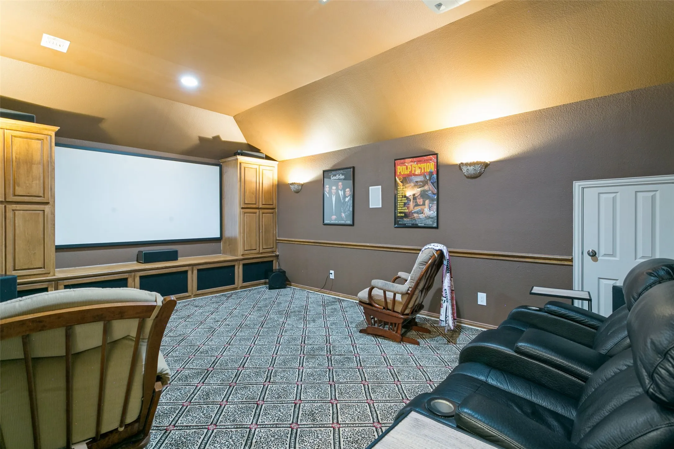 Dedicated media room featuring a large projection screen, built-in cabinetry, patterned carpet flooring, wall sconces, and crown molding