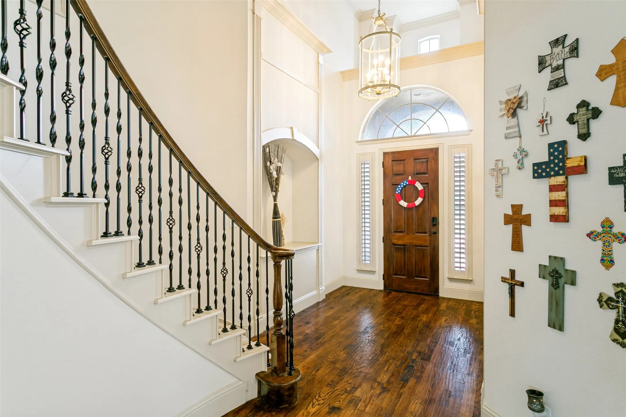 Grand entryway featuring rich wood-finish flooring, a curved staircase with ornate iron balusters, a solid wood entry door, and an arched transom window