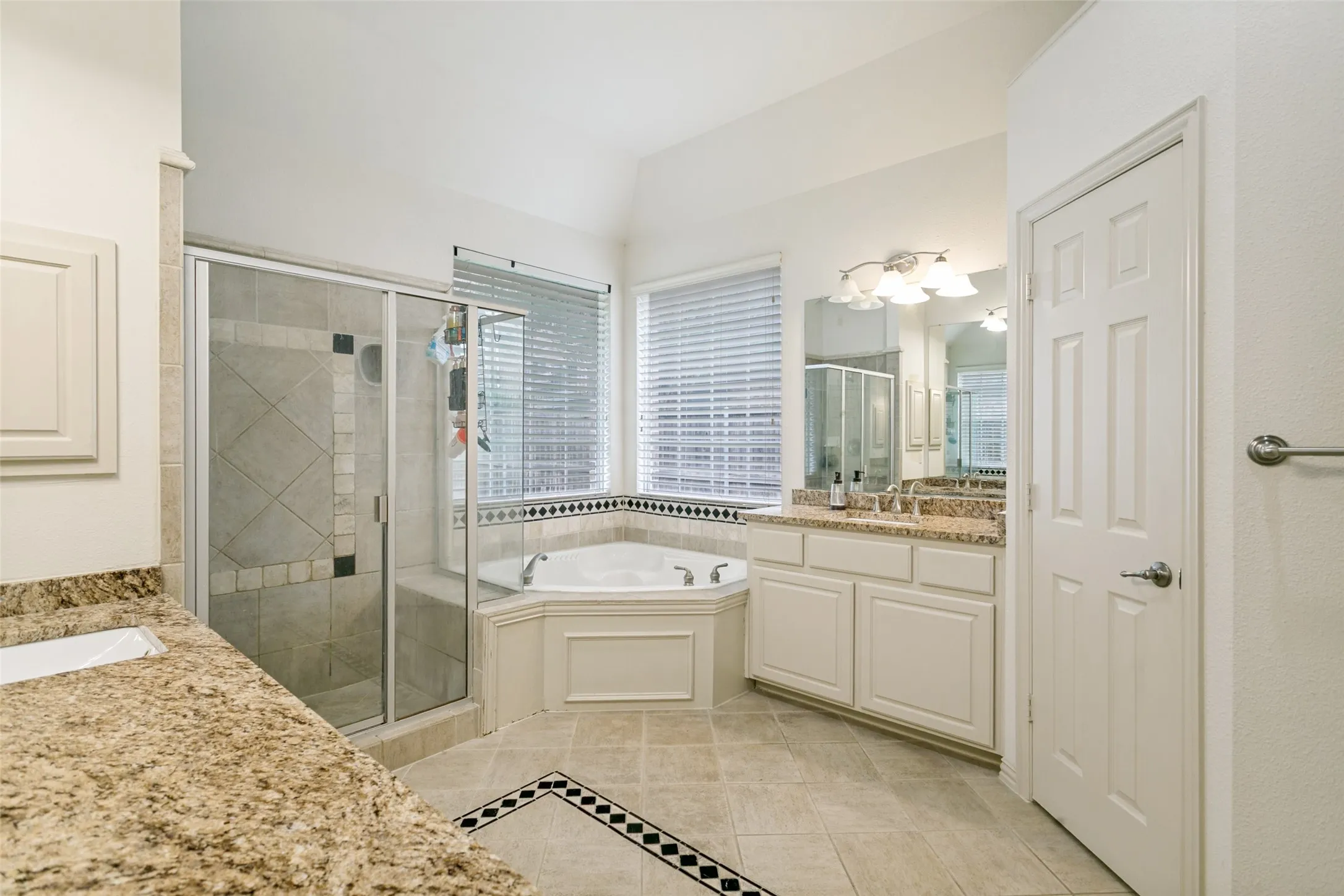Bathroom featuring a corner jetted tub, a separate glass-enclosed shower with tile surround, and a dual vanity with granite countertops