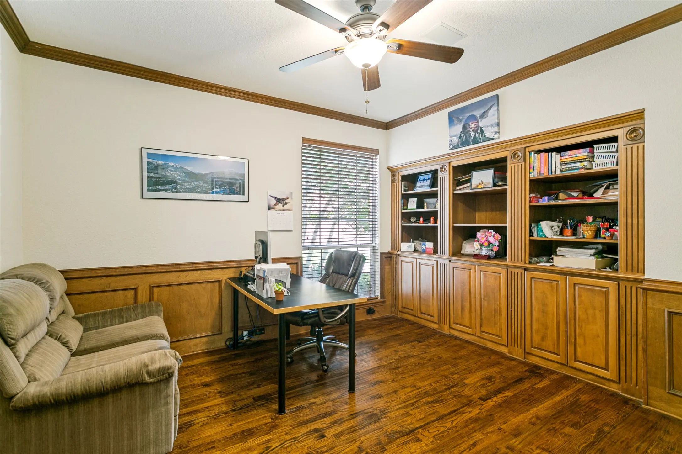 Room featuring extensive built-in cabinetry, wood-finish flooring, wood paneling, crown molding, and a ceiling fan with integrated lighting