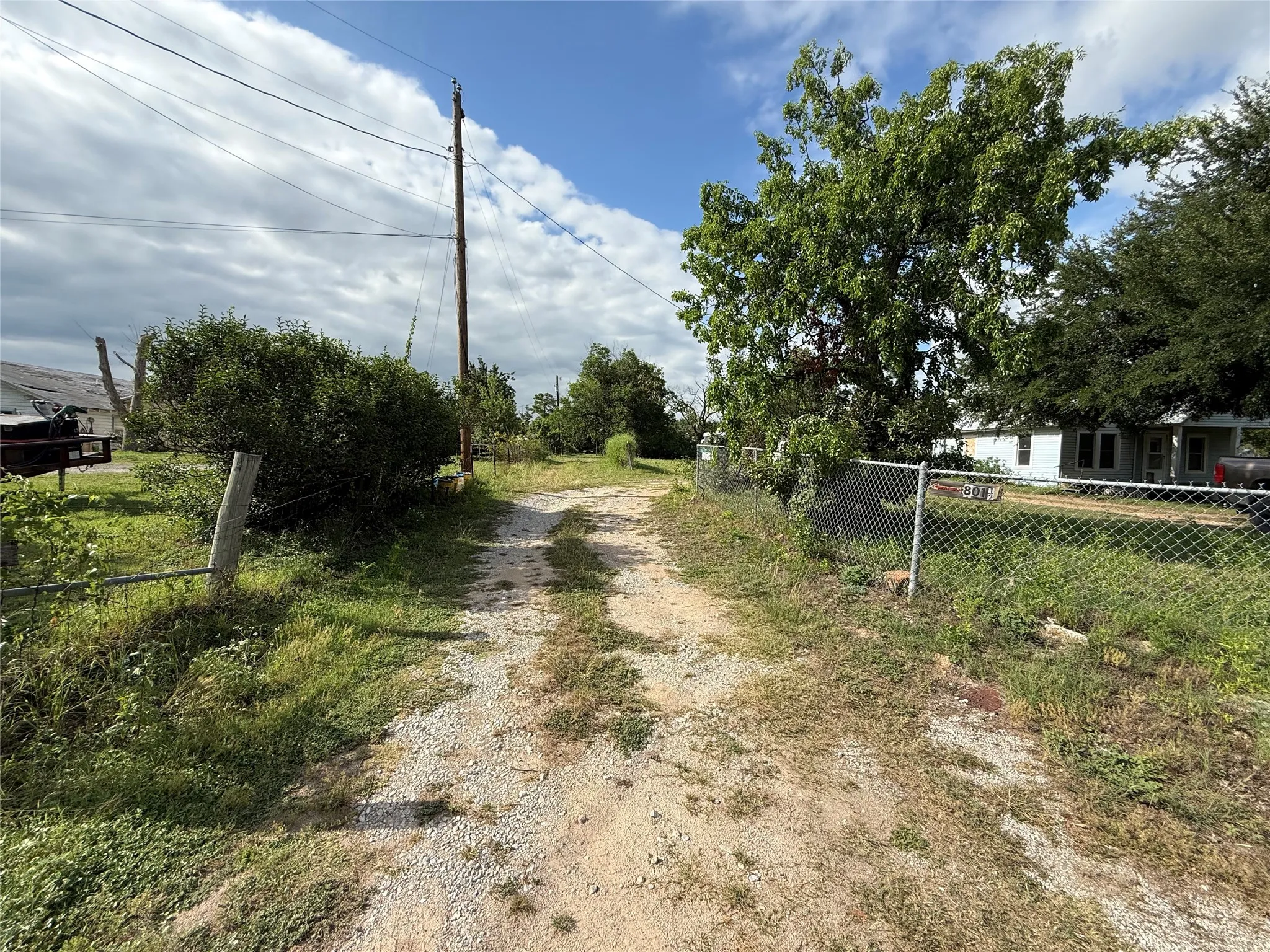 Gravel driveway with a chain-link fence and mature trees