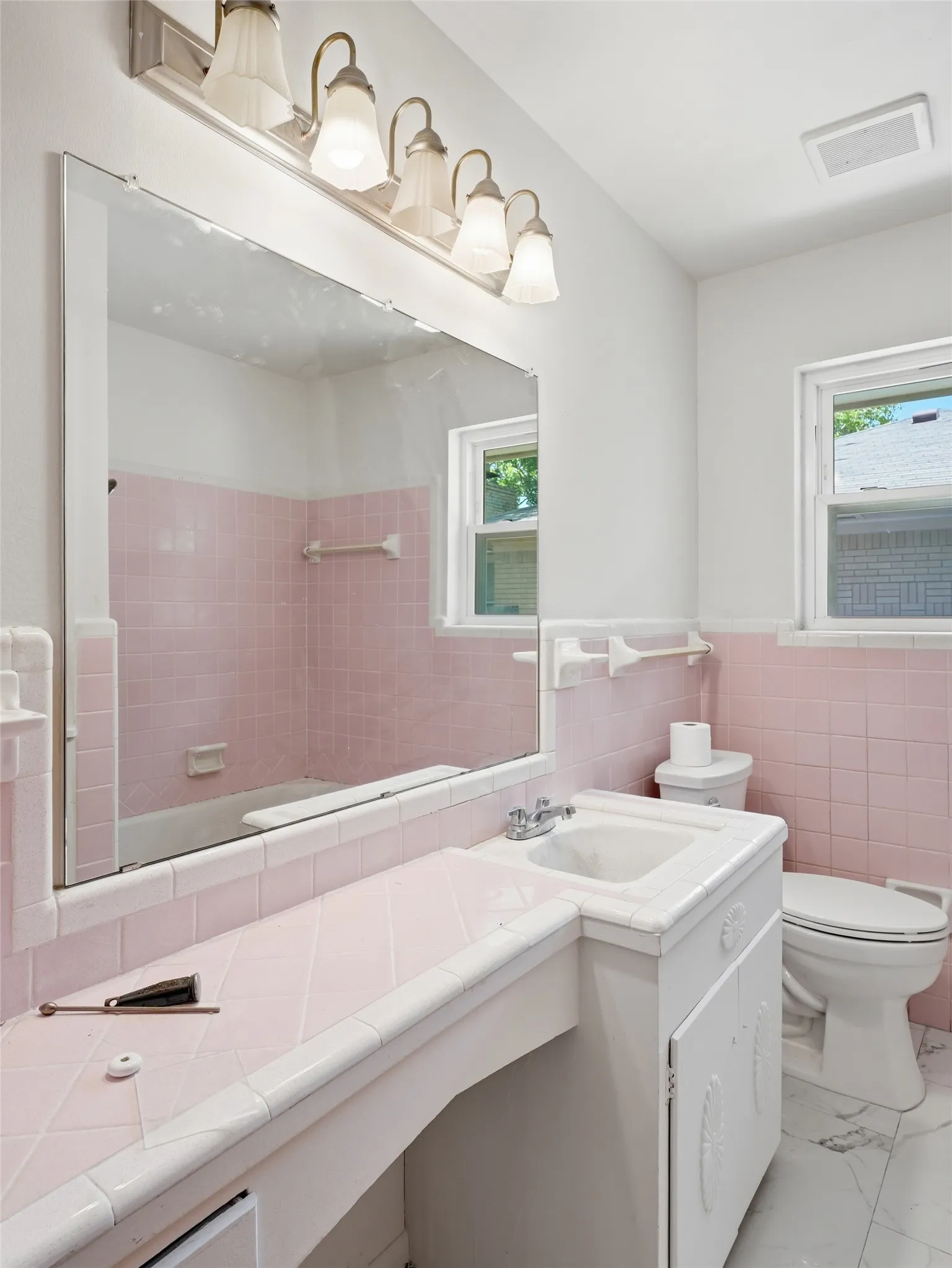 Bathroom featuring a full vanity mirror, five-light fixture, built-in vanity with tiled countertop, tiled shower enclosure, and white ceramic tile flooring
