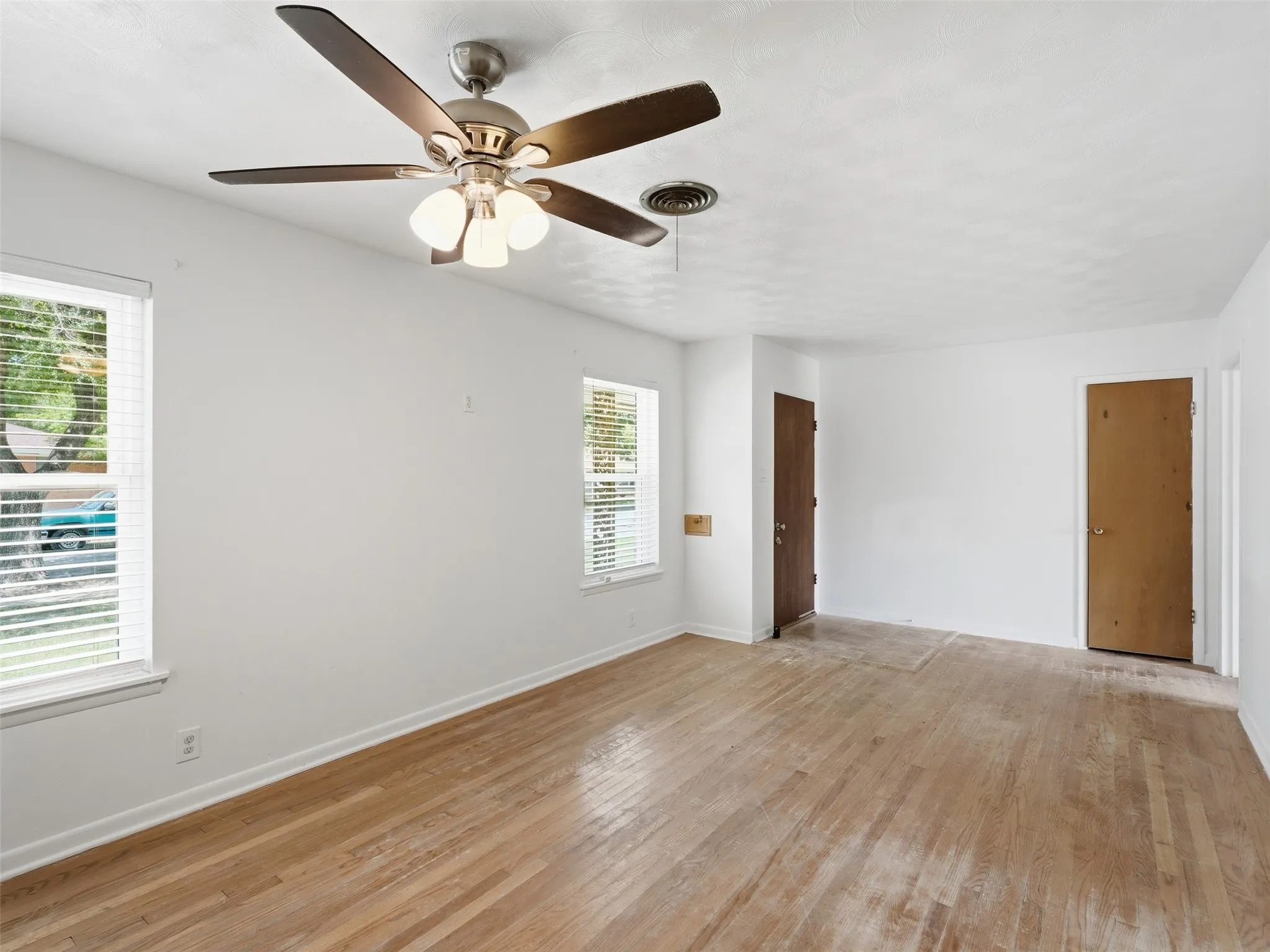 Bright interior space featuring wood-finish flooring, two windows with blinds, a ceiling fan with integrated lighting, and white painted walls