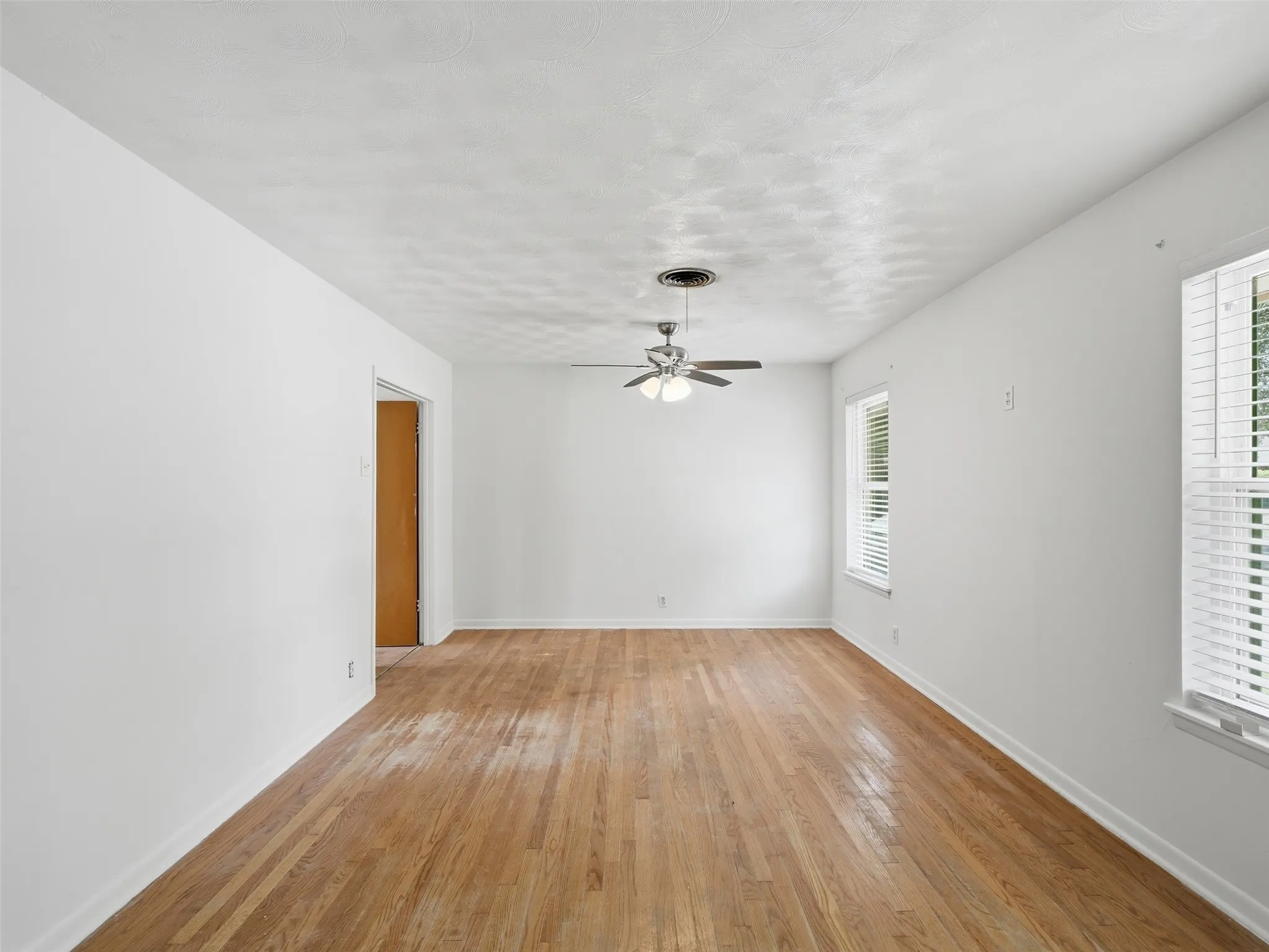 Bright interior space featuring wood-finish flooring, white wall paint, and a ceiling fan with integrated lighting