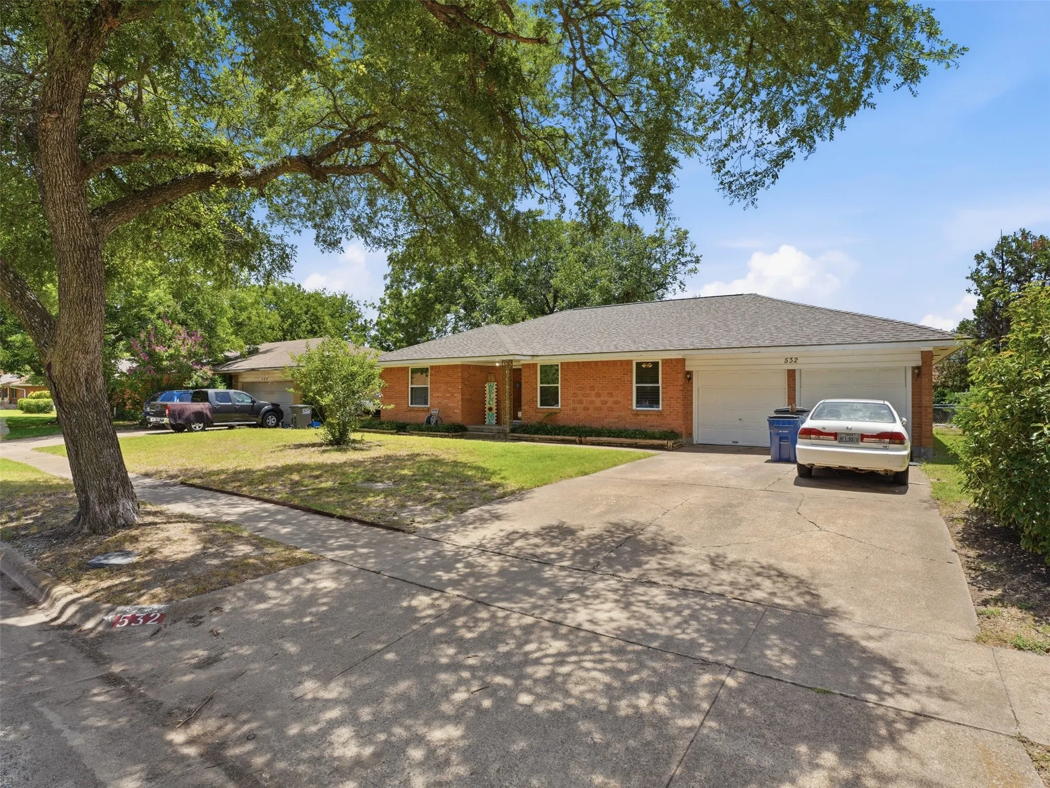 Brick exterior residence with a dual-bay garage, concrete driveway, and mature landscaping