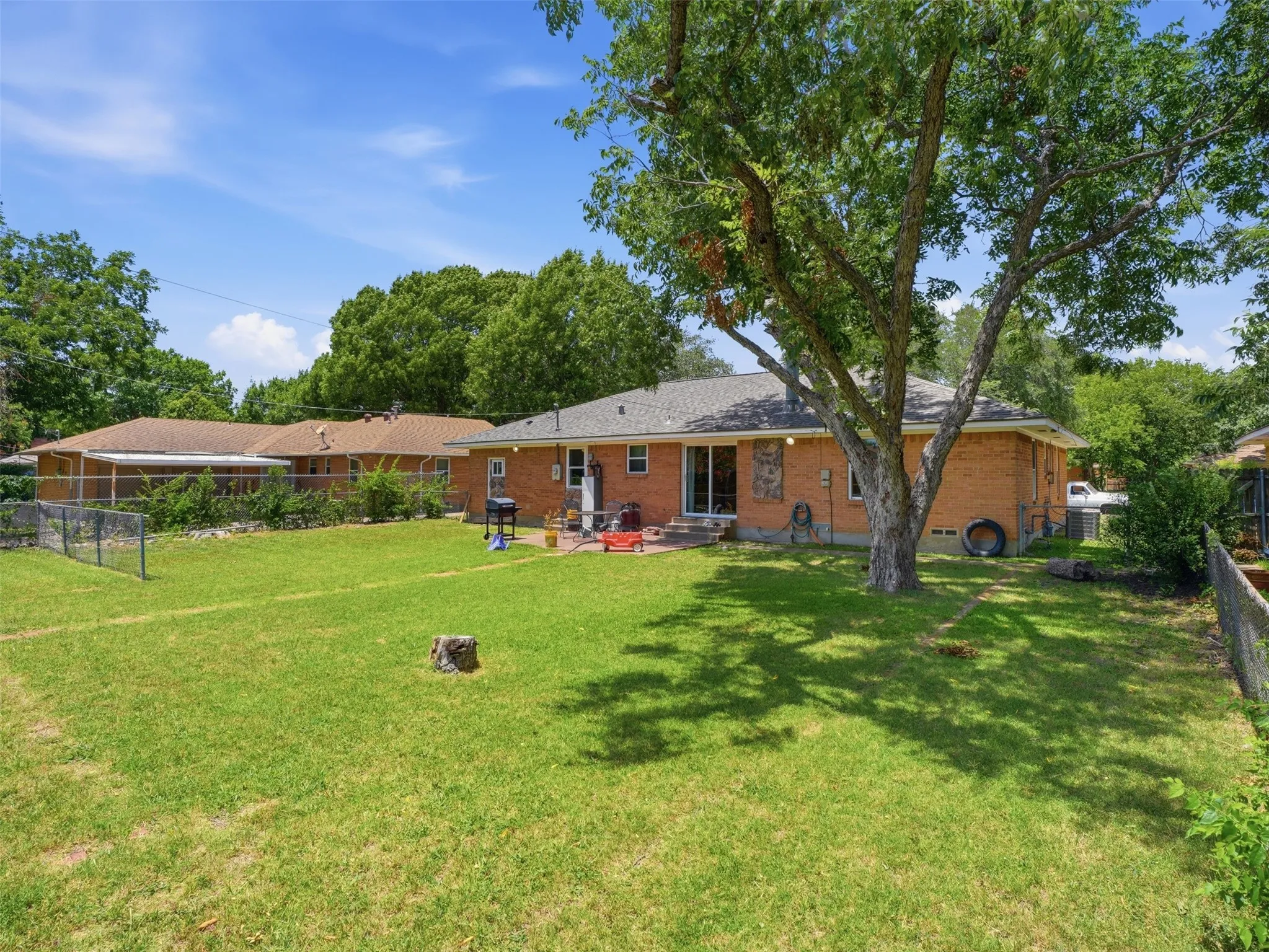 Expansive green lawn with a mature shade tree and a brick exterior home