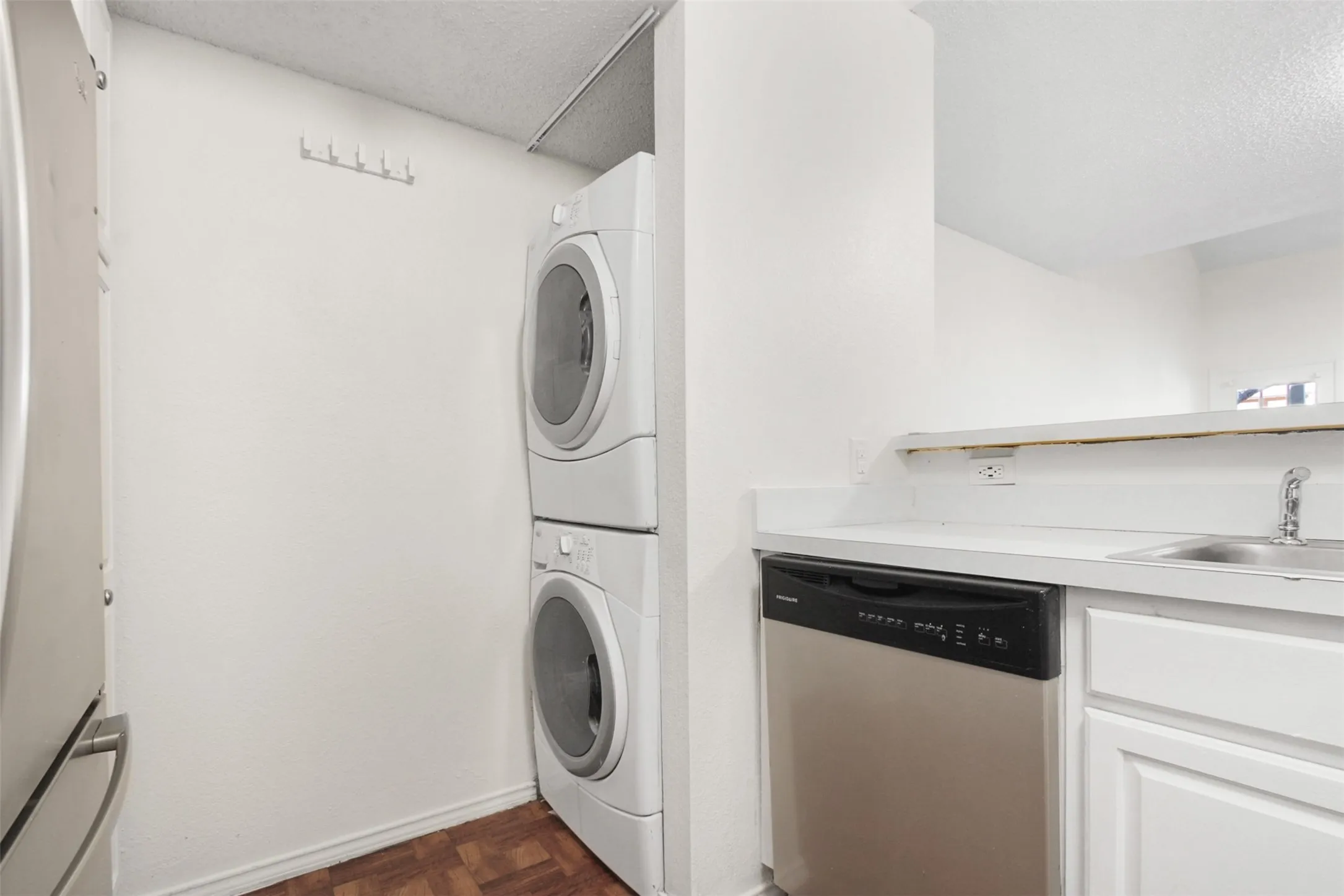 Compact laundry area featuring a stacked washer and dryer, wood-finish flooring, and a wall-mounted hook rack