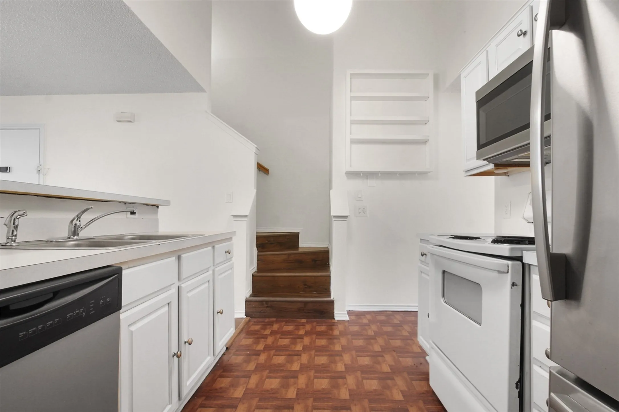 Kitchen featuring white cabinetry with brass hardware, a double basin stainless steel sink, a stainless steel dishwasher, and a white electric range with an overhead microwave