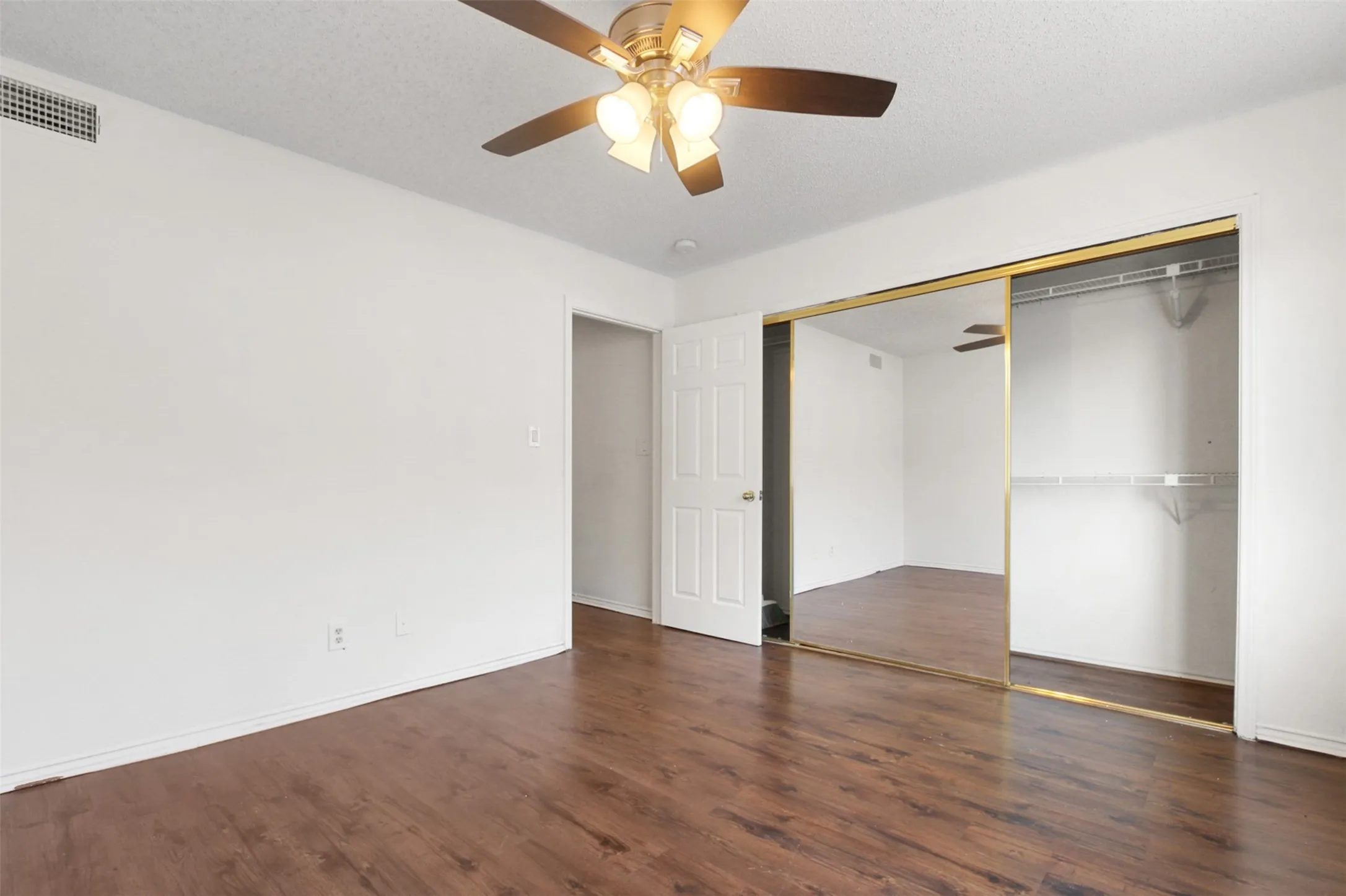 Interior room featuring wood-finish flooring, a ceiling fan with integrated lighting, and a mirrored closet with gold-tone framing
