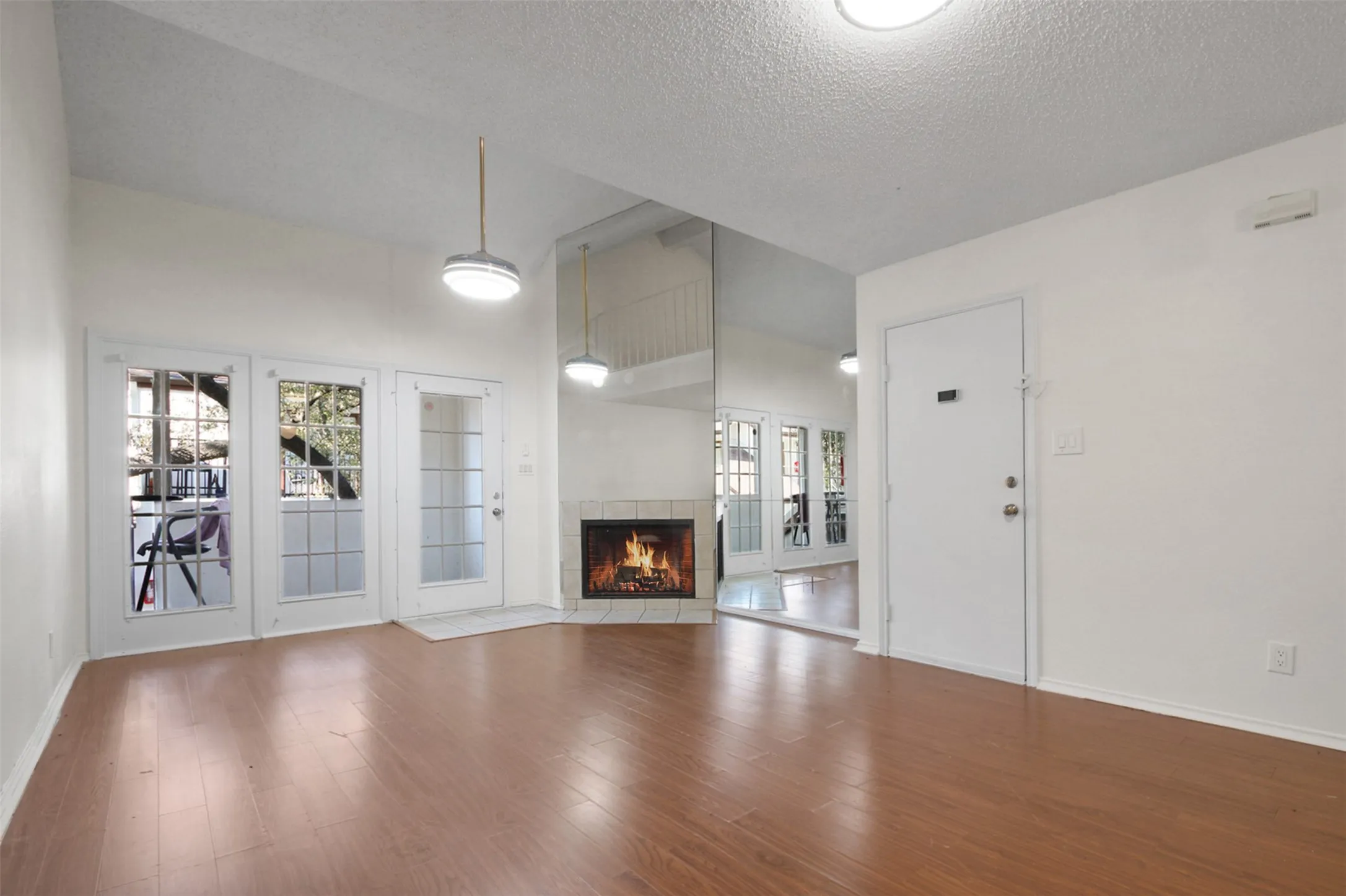 Spacious living area featuring wood-finish flooring, a corner fireplace with a light-toned tile surround, and multiple French doors providing exterior access