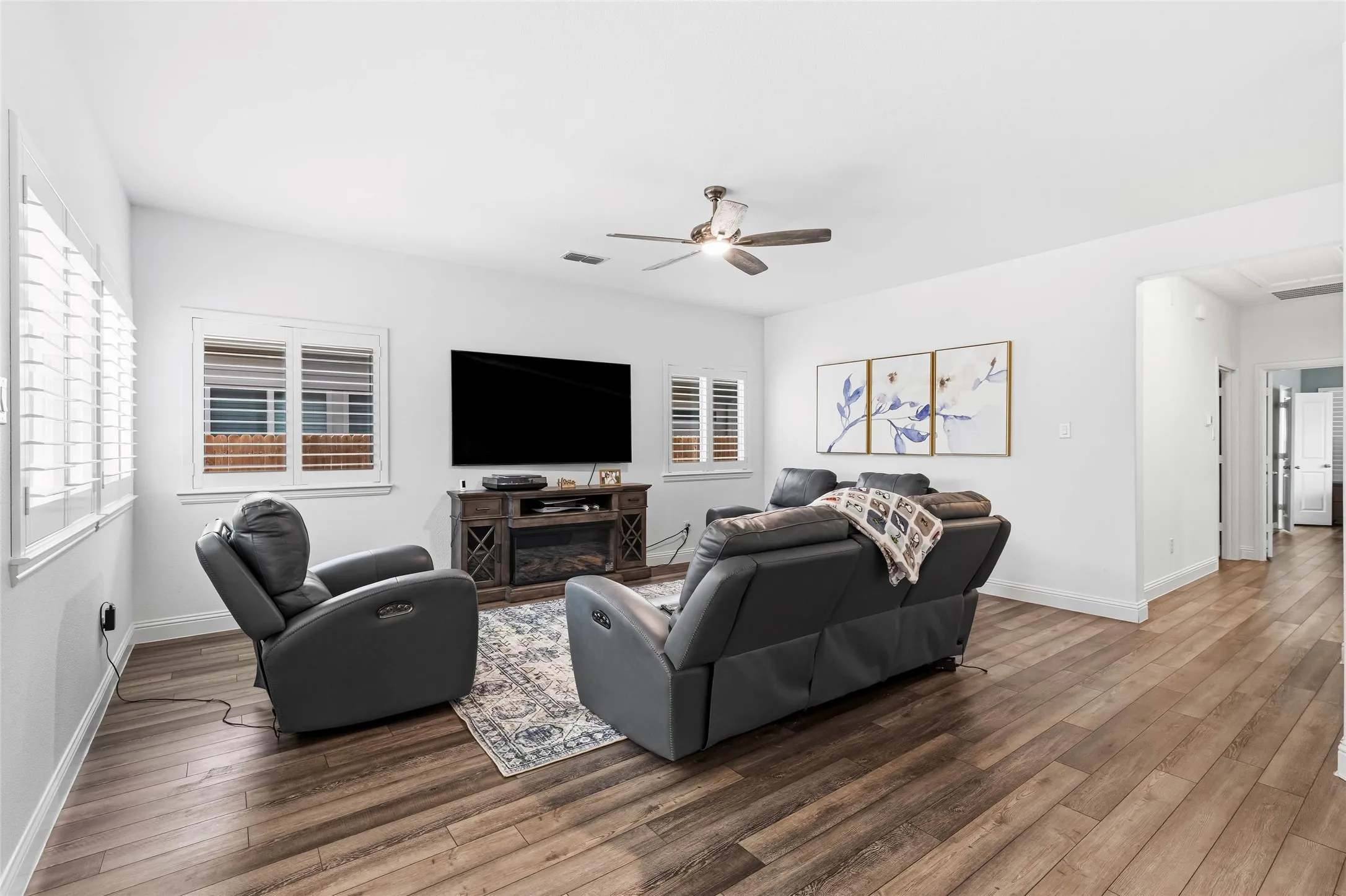 Spacious living area featuring wood-finish flooring, white walls, and a ceiling fan