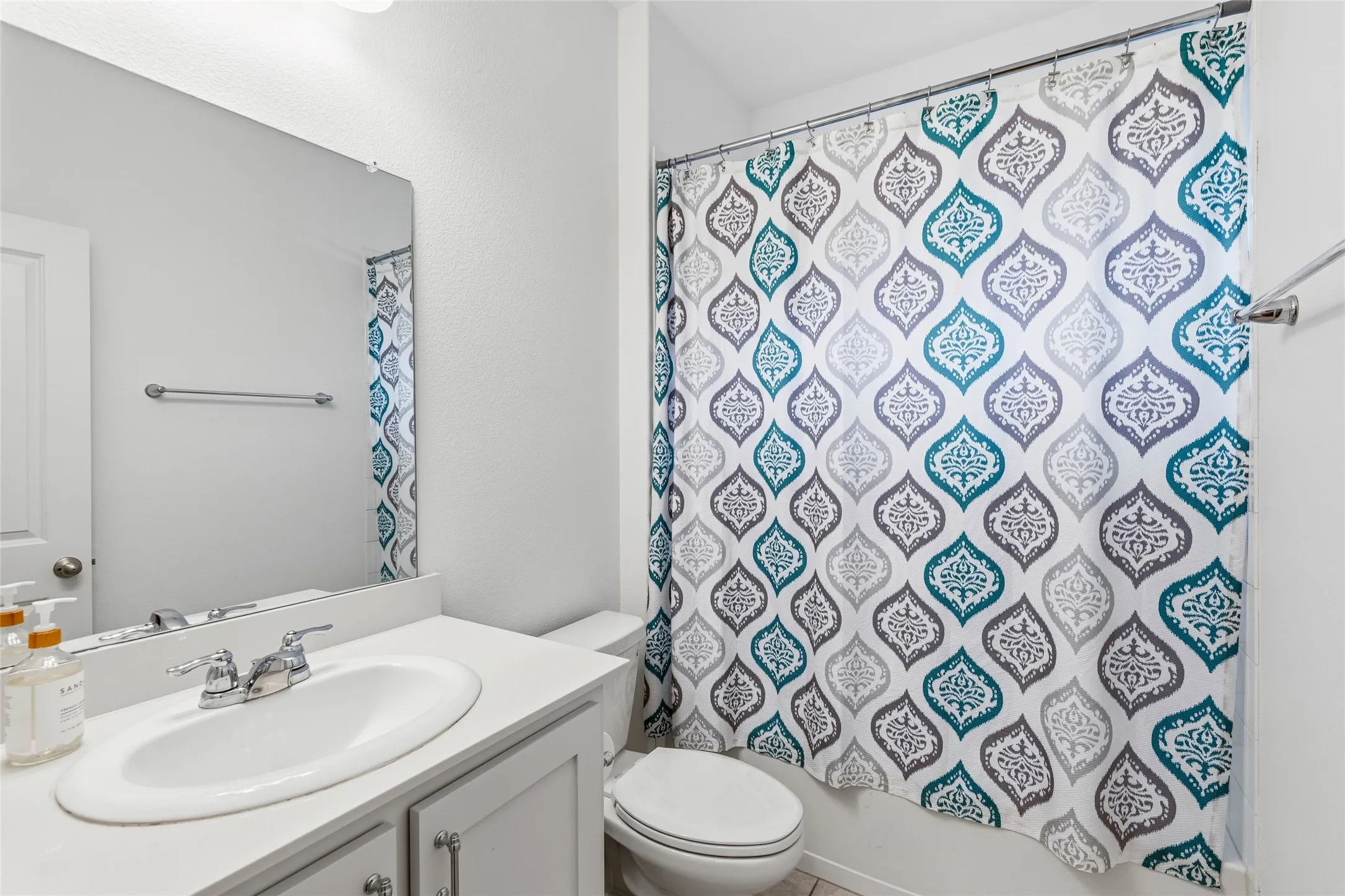 Bathroom featuring a single vanity with an integrated sink and chrome fixtures, light-toned cabinetry with silver hardware, a wall-mounted mirror, and a toilet