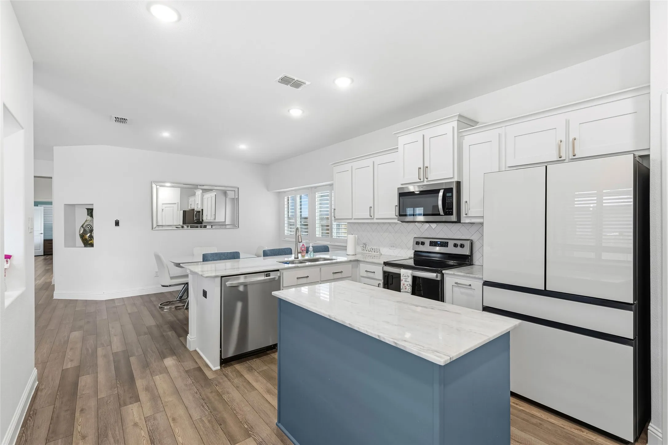 Modern kitchen featuring white cabinetry, stainless steel appliances, and a central island with a blue base