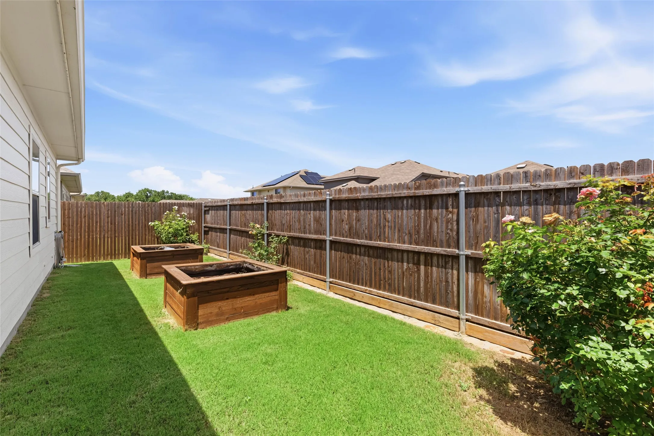 Private backyard featuring a manicured lawn, two raised garden beds, and a wood privacy fence