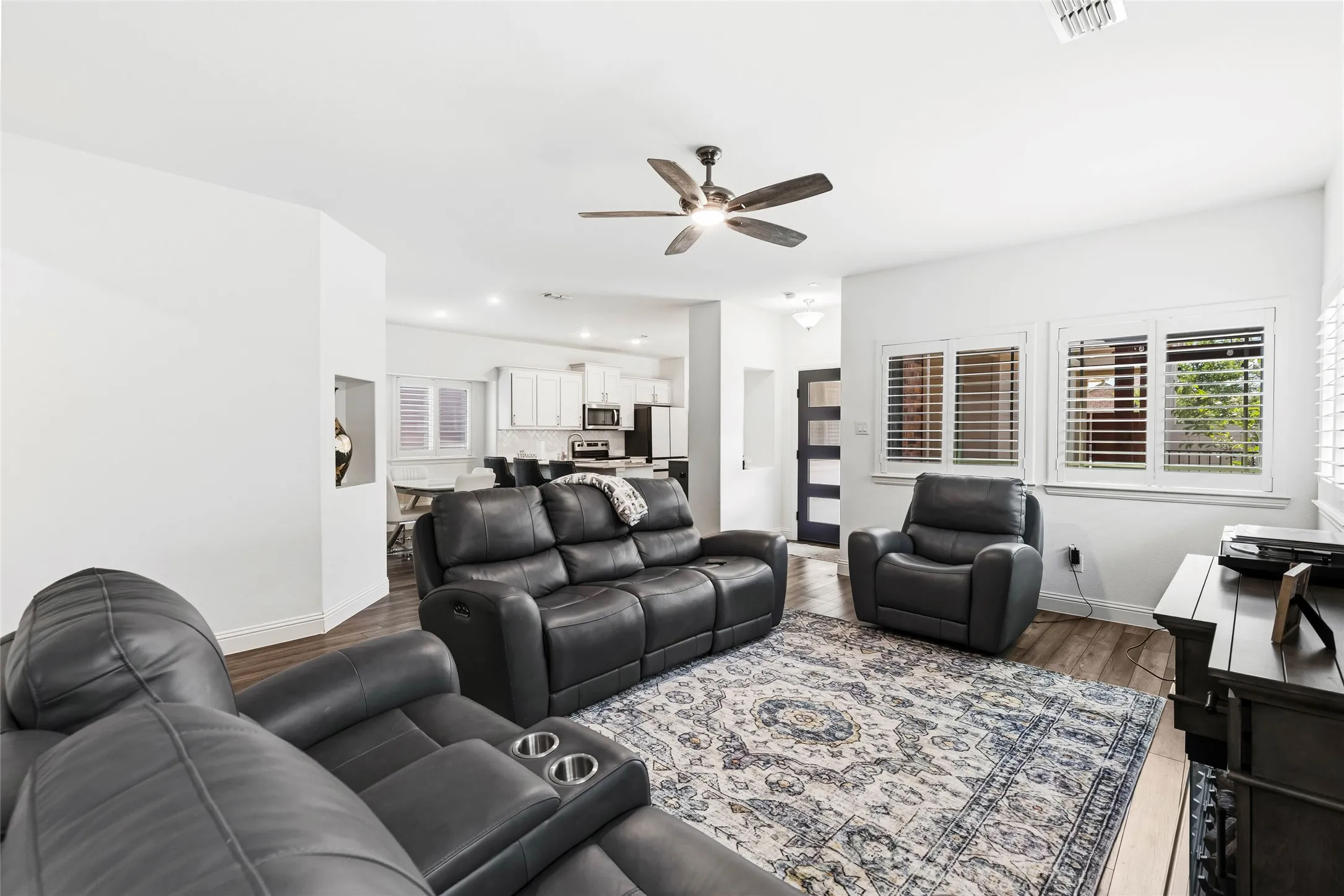 Open-concept living area featuring wood-finish flooring, white walls, and a ceiling fan